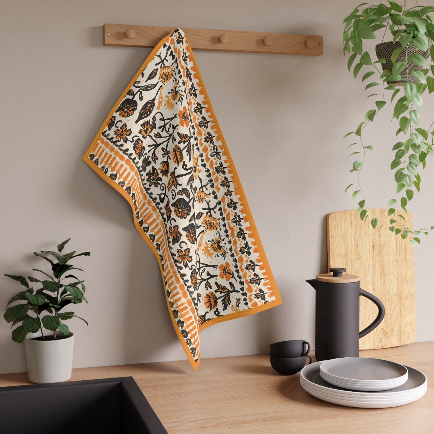 Decorative towel with floral pattern hanging on a wooden rack above a kitchen counter with utensils and plants.