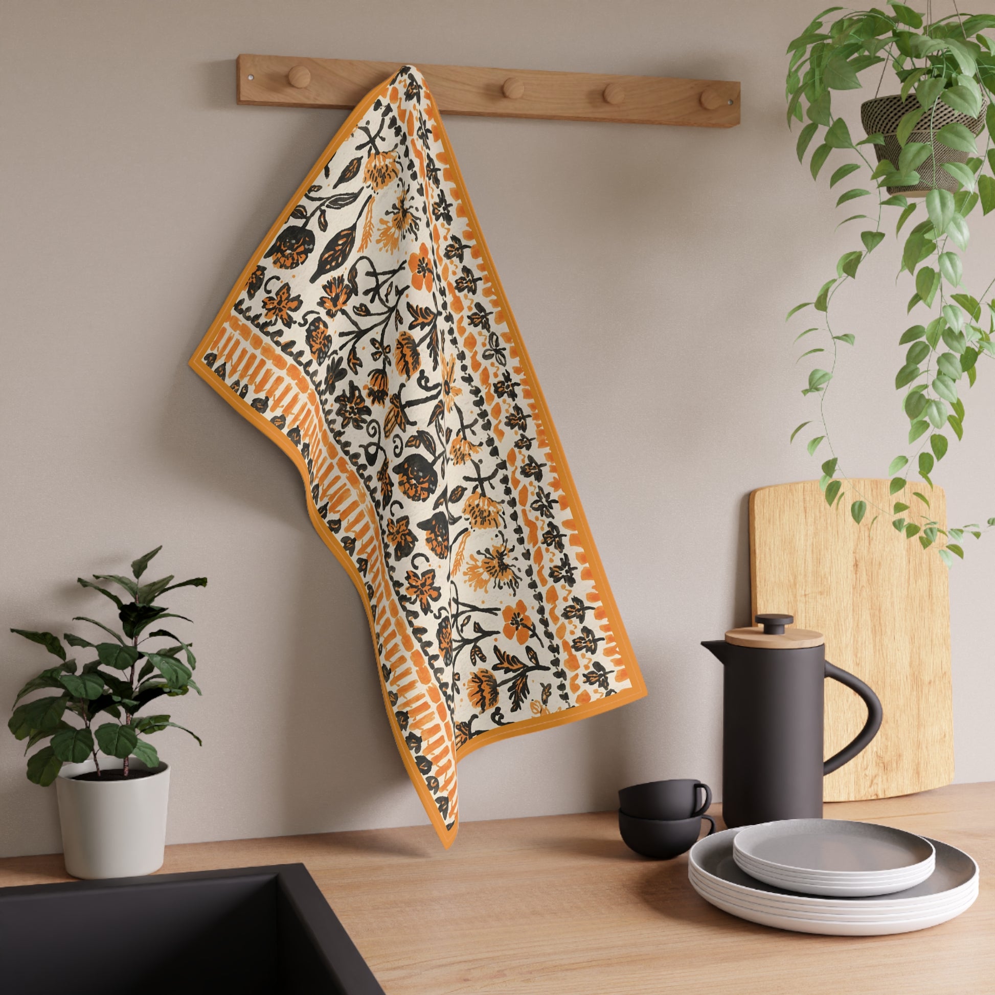 Decorative towel with floral pattern hanging on a wooden rack above a kitchen counter with utensils and plants.
