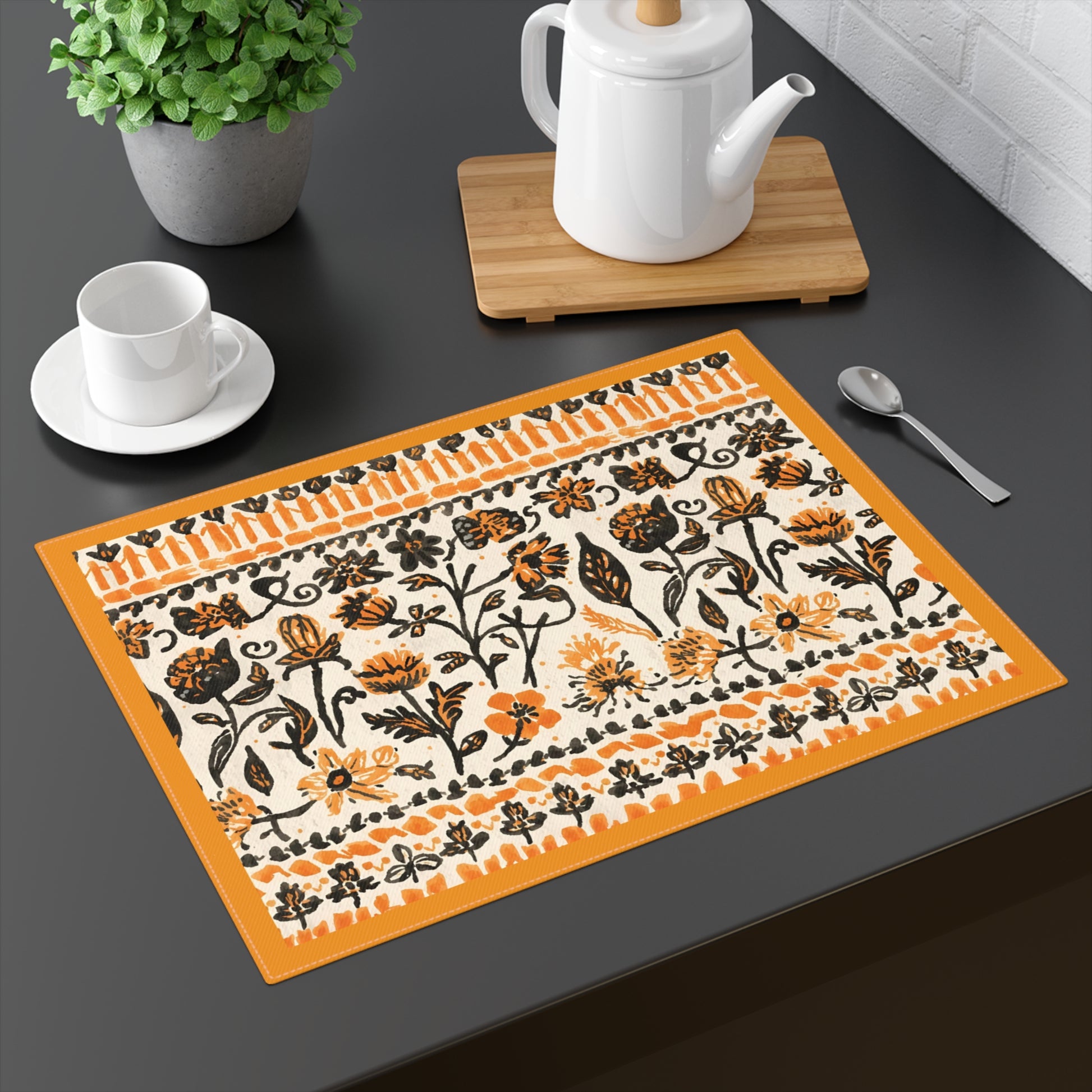 Fall Flowers placemat, with a boho orange and black floral pattern, is printed on a cotton twill placemat fabric, sits on a dark table with tea set.