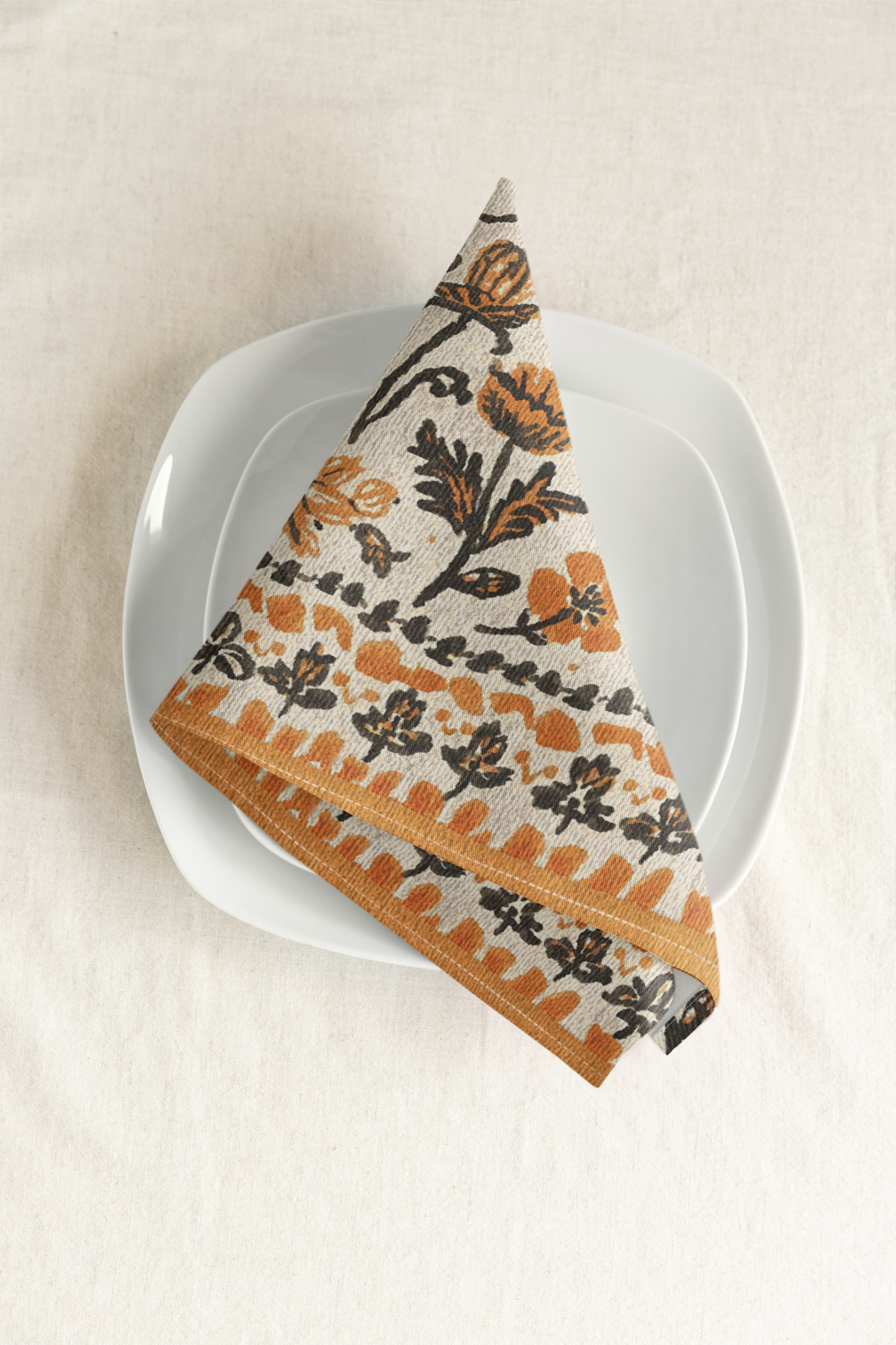 Fall Flowers napkin, with a boho orange and black floral pattern, is printed on a cotton twill reusable napkin fabric, on a white plate against a beige background