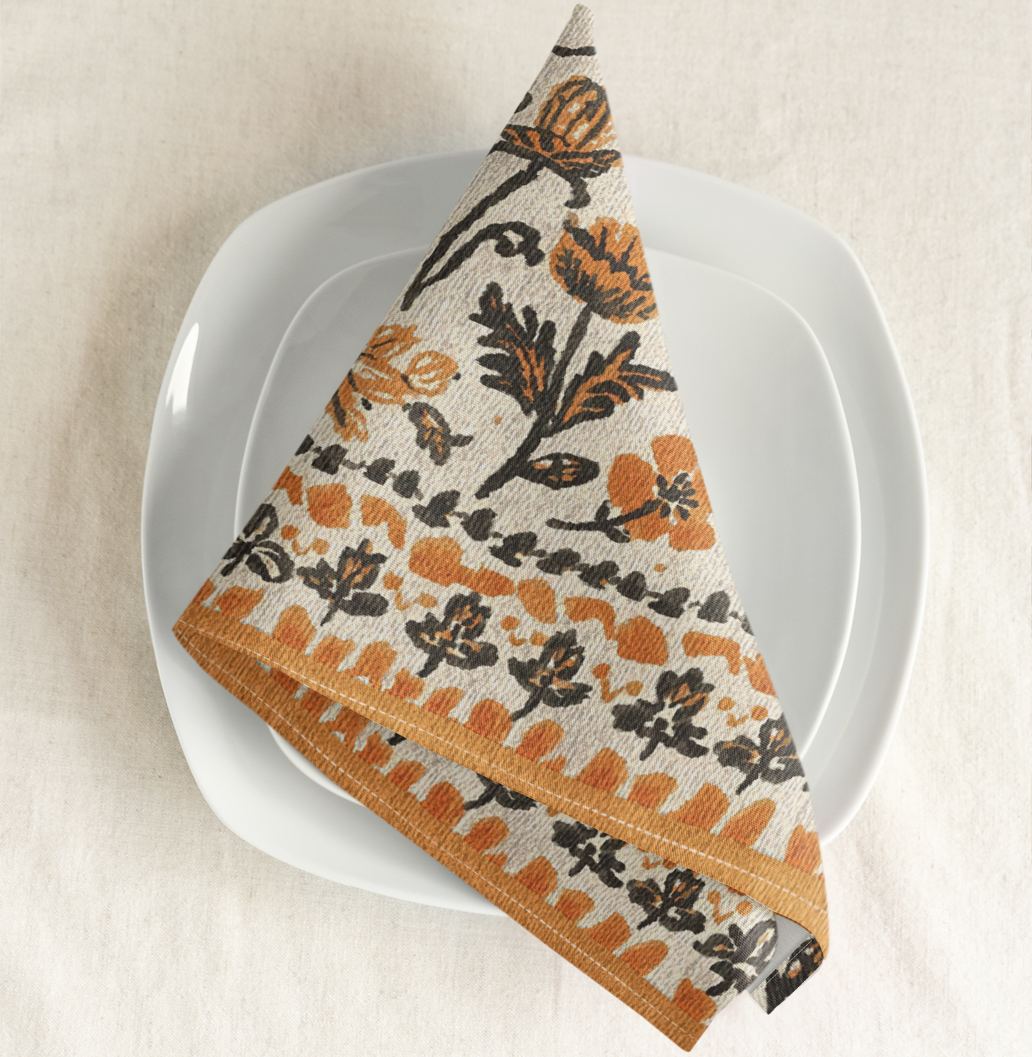 Fall Flowers napkin, with a boho orange and black floral pattern, is printed on a cotton twill reusable napkin fabric, on a white plate with a beige background