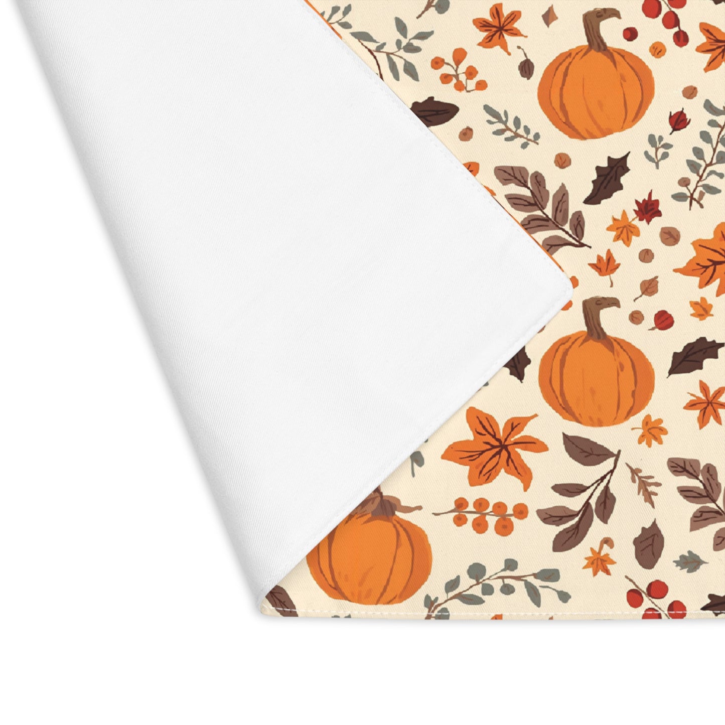 Fall Leaves and Pumpkins placemat has brown and orange fall leaves with orange pumpkins on a beige background printed on the table runner cotton twill fabric. The placemat corner is folded over to reveal the white backside and is shown on on a white background