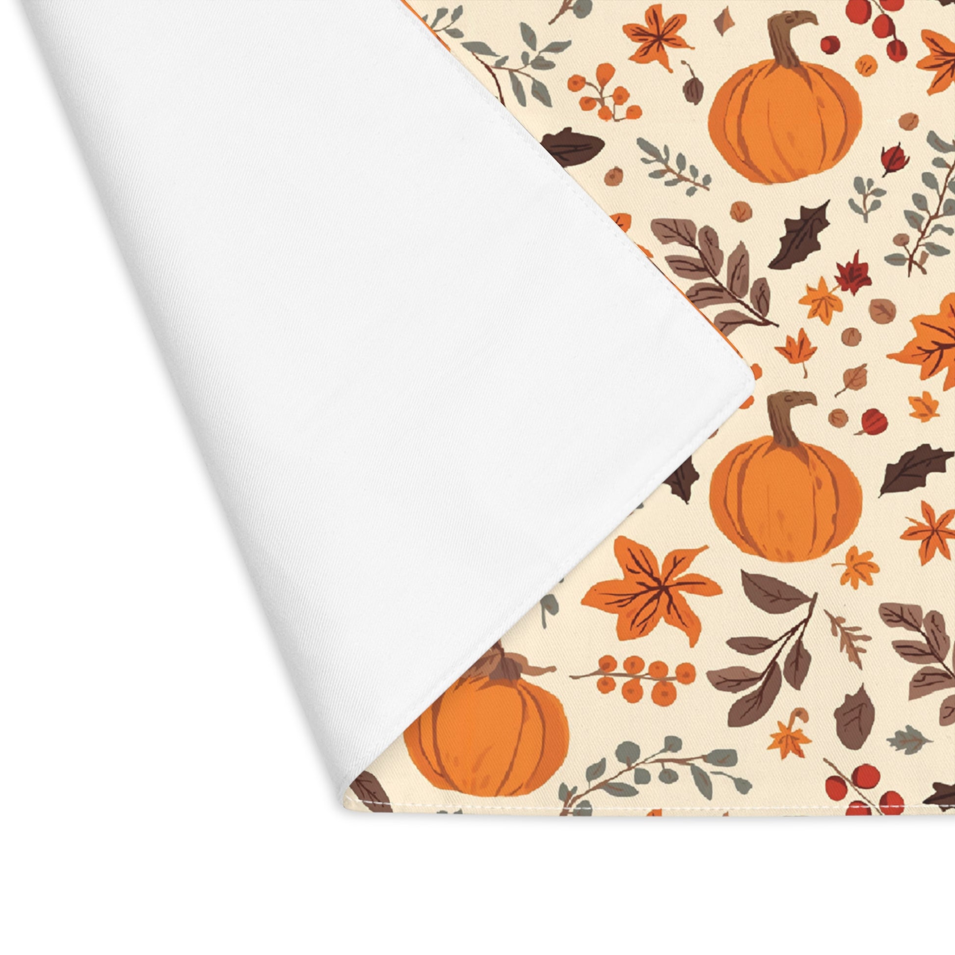 Fall Leaves and Pumpkins placemat has brown and orange fall leaves with orange pumpkins on a beige background printed on the table runner cotton twill fabric. The placemat corner is folded over to reveal the white backside and is shown on on a white background