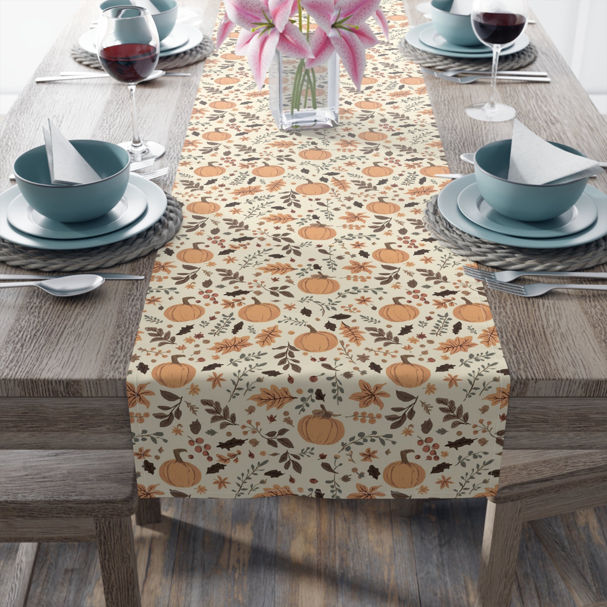 Fall Leaves and Pumpkins table runner has brown and orange fall leaves with orange pumpkins with a beige background design printed on the table runner shown on a table setting on a wooden table.