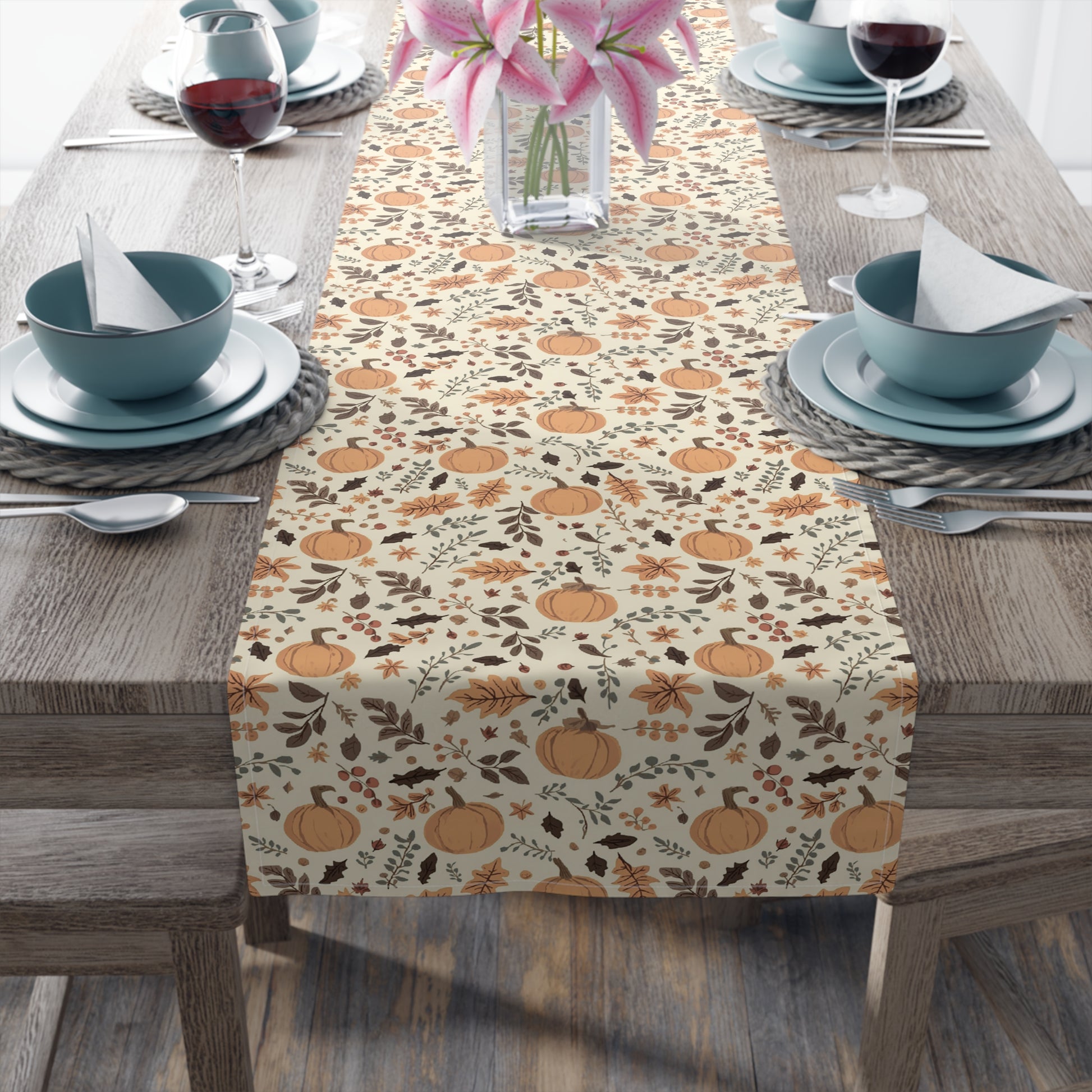 Fall Leaves and Pumpkins table runner has brown and orange fall leaves with orange pumpkins on a beige background design printed on the table runner shown on a table setting on a wooden table.