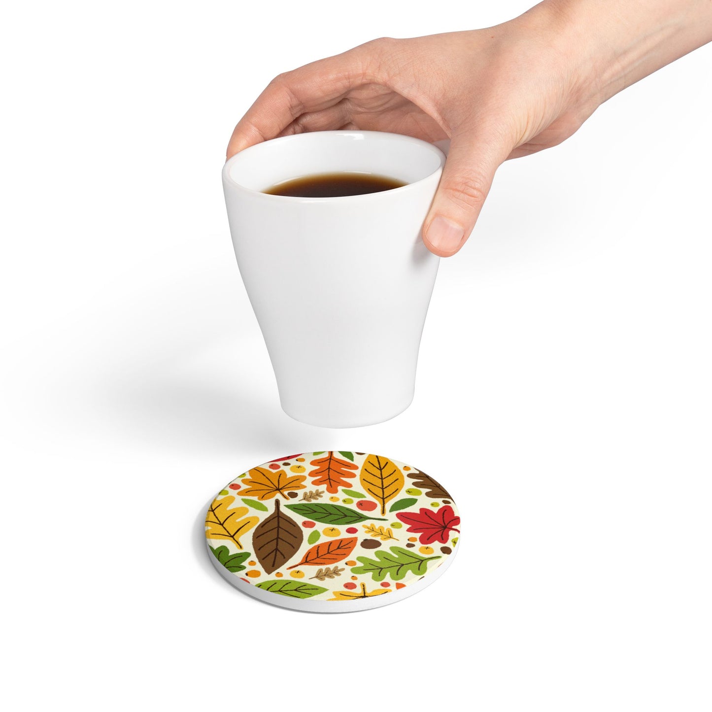 Hand holding a white mug over our round Fall Leaves ceramic tile coaster with a colorful leaf-patterned on top of coaster tile on a white background.