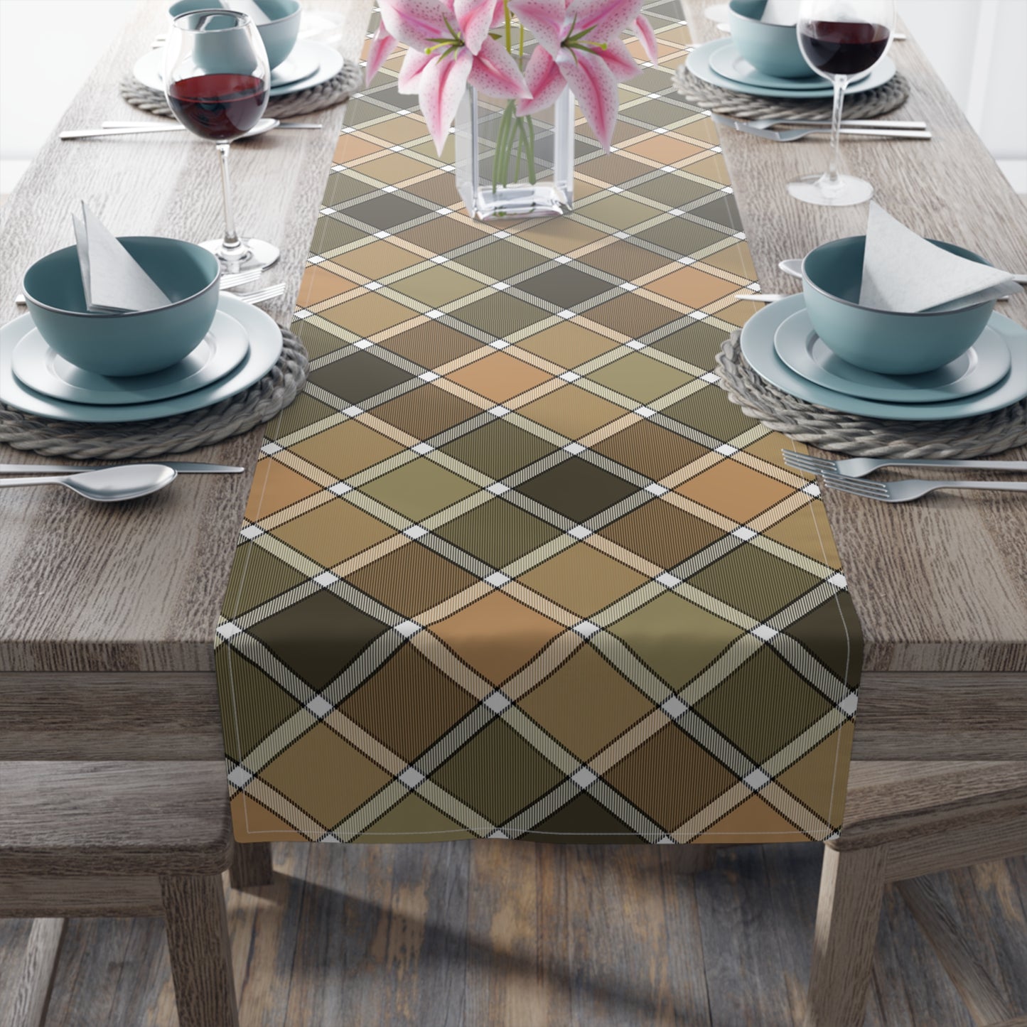 Our cotton twill Fall Plaid table runner has brown, green, orange patterned colors. The table runner is sitting table with blue dishes and flower vase.