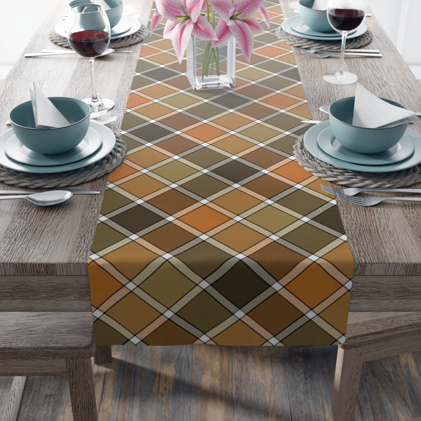Our Fall Plaid table runner has brown, green, orange plaid patterned colors. The table runner is on a dining table with glasses, and plates.
