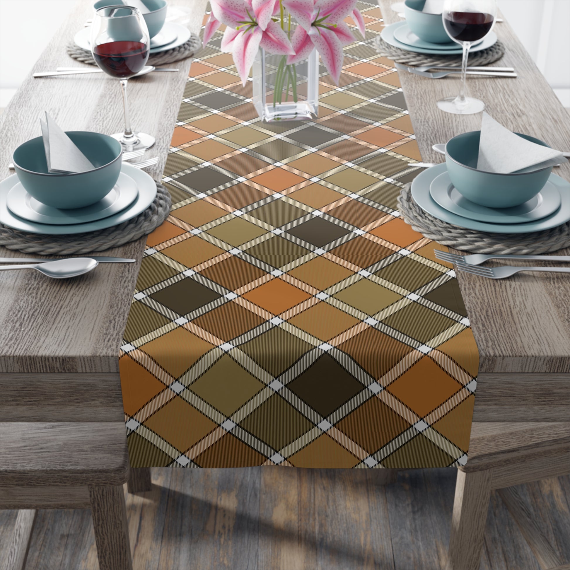 Our Fall Plaid table runner has brown, green, orange plaid patterned colors. The table runner is on a dining table with glasses, and plates.