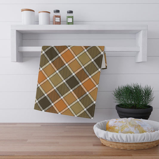 Fall colored plaid kitchen tea towel hanging on a wooden shelf with a plant and basket in the foreground.