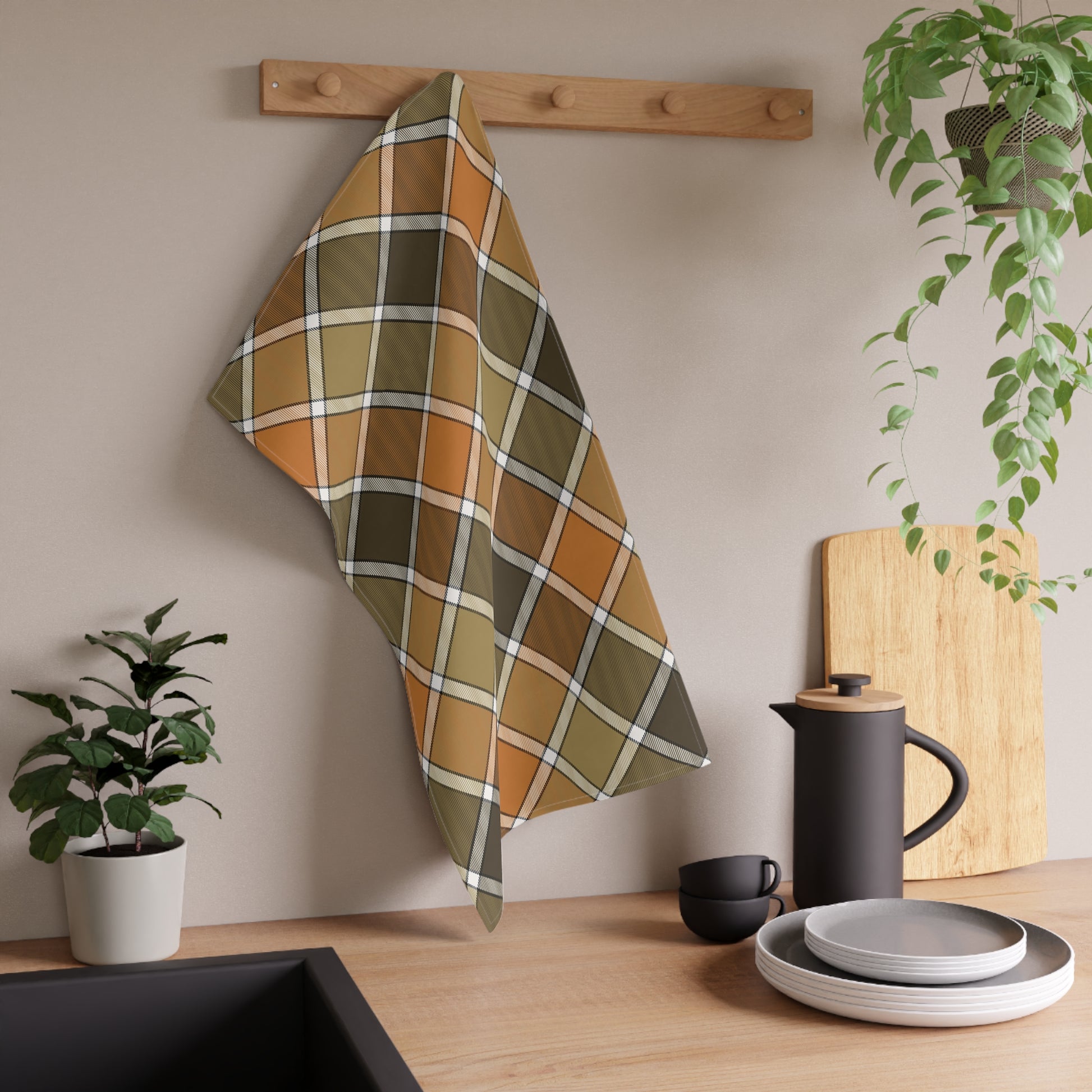 Orange, green and gold plaid kitchen tea towel hanging on a wooden rack with kitchen items and plants in the background
