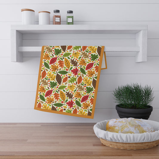 Colorful leaf-patterned towel hanging on a wooden shelf with a plant and basket in the foreground.