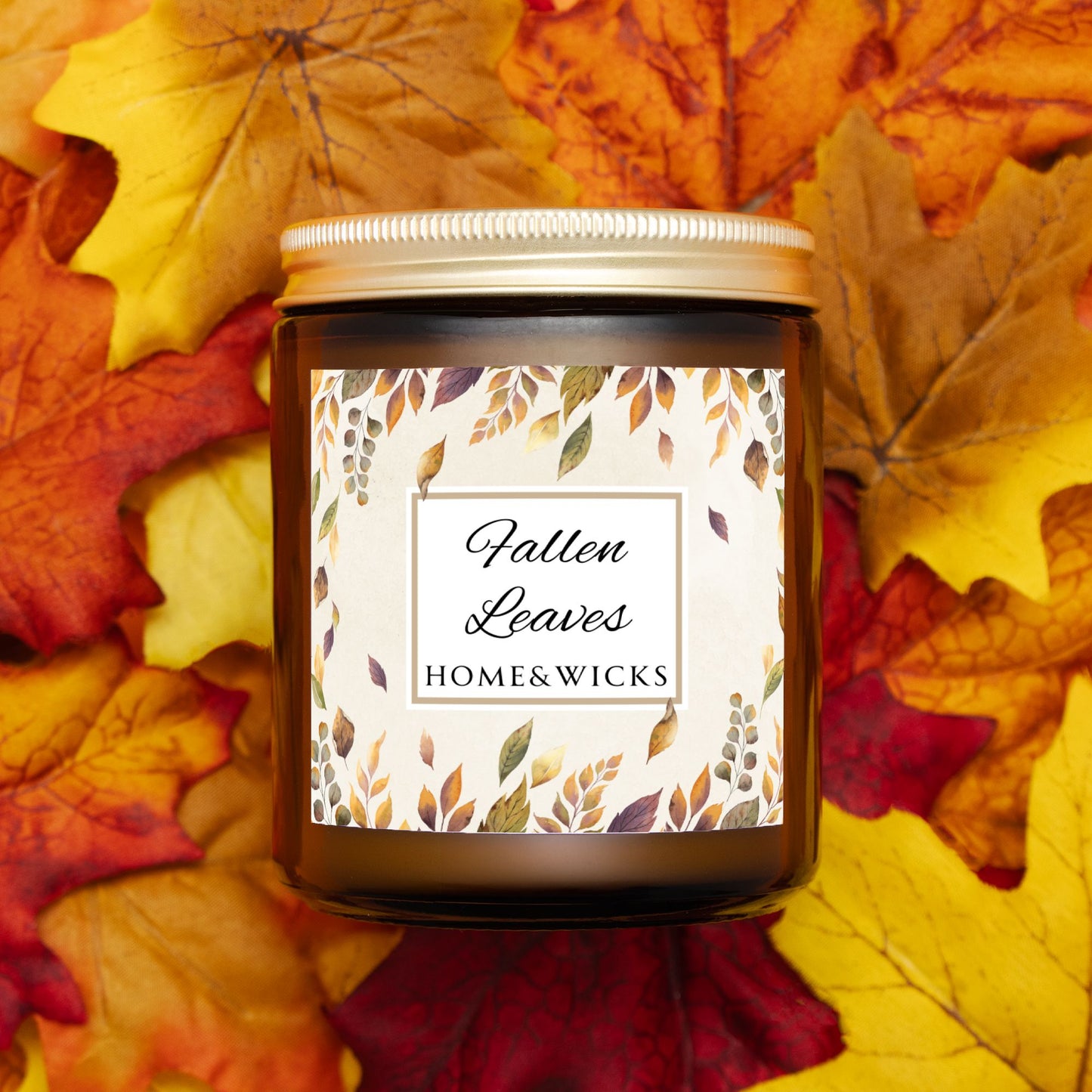 Amber candle jar with gold lid labeled 'Fallen Leaves' by HOME & WICKS on a bed of autumn leaves.