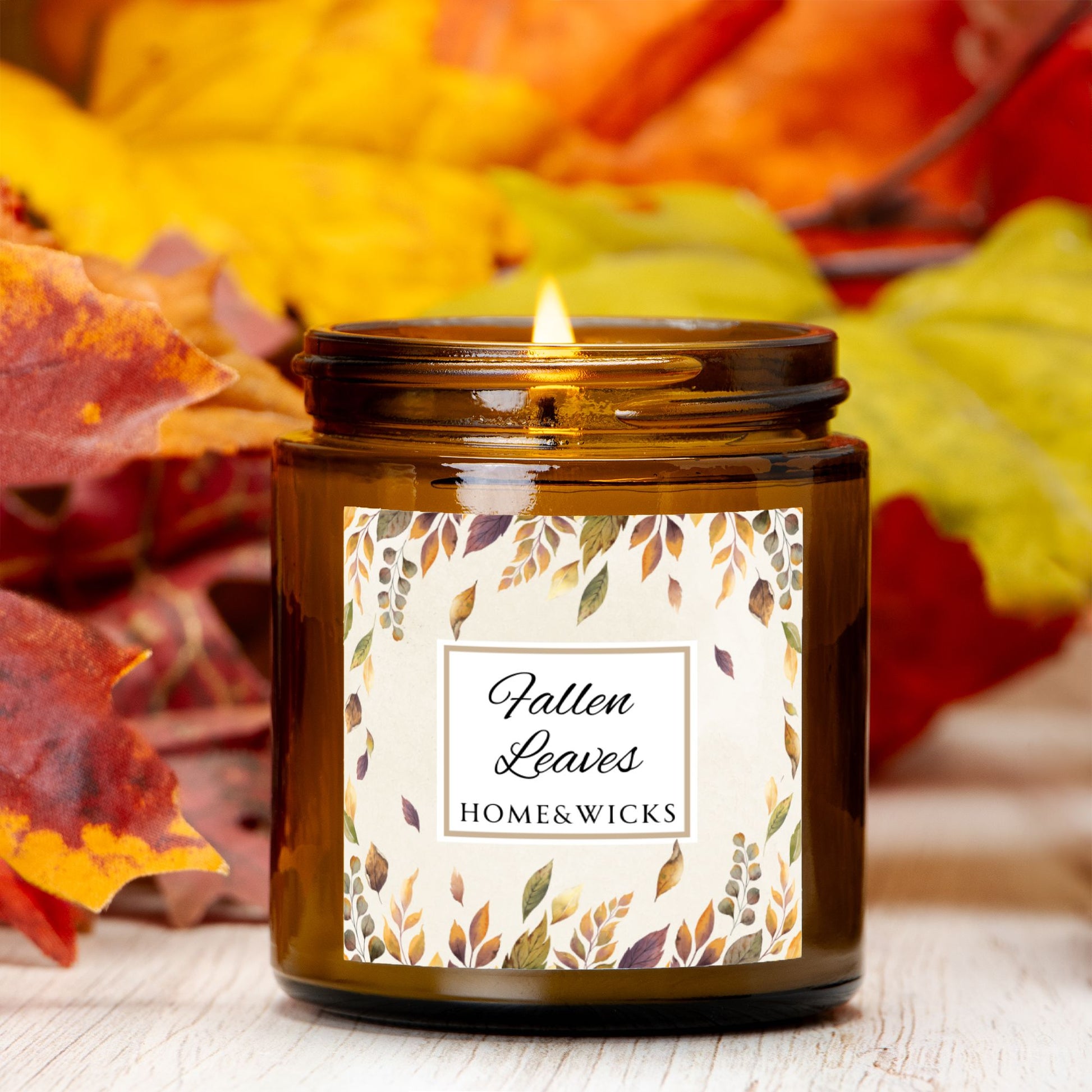 Lit candle in a jar labeled 'Fallen Leaves' from Home & Wicks with autumn leaves in the background.