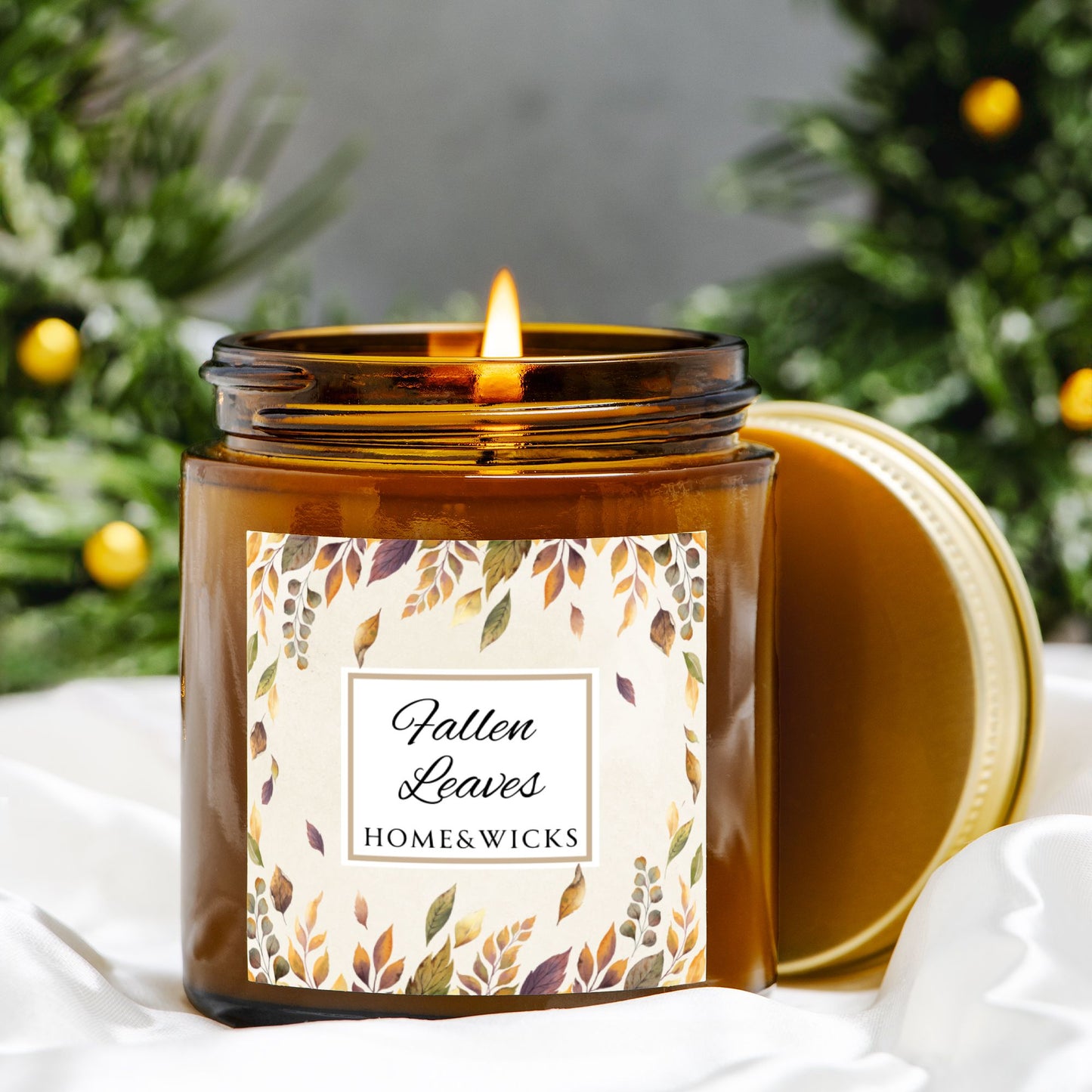 Lit candle in an amber jar with a 'Fallen Leaves' label, surrounded by greenery.