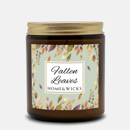 Amber glass candle jar with a gold lid with a brown, gold and green 'Fallen Leaves' label on a white background by Home & Wicks