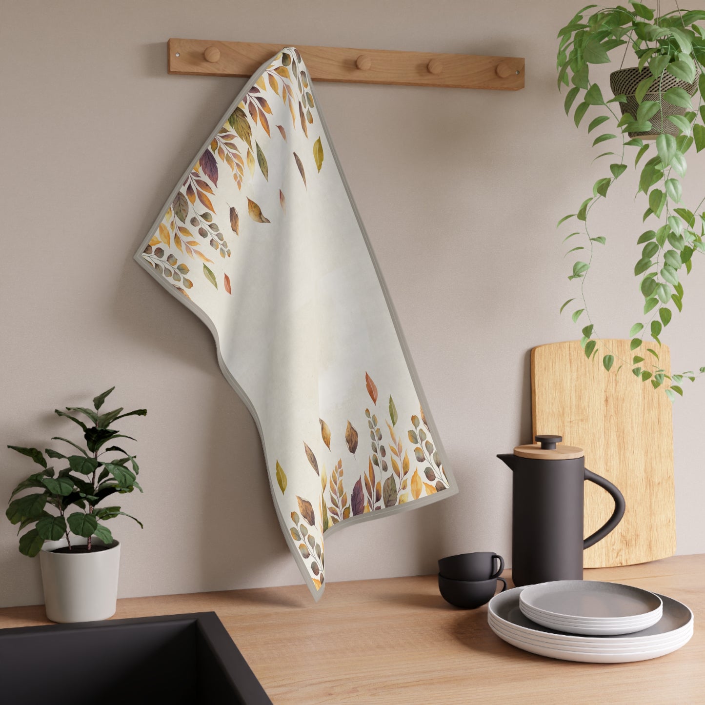 Decorative kitchen tea towel with leaf pattern hanging on a wooden rack in a kitchen setting.