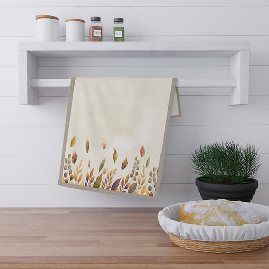 Decorative kitchen tea towel with autumn leaf pattern on a wooden surface with a shelf in the background.