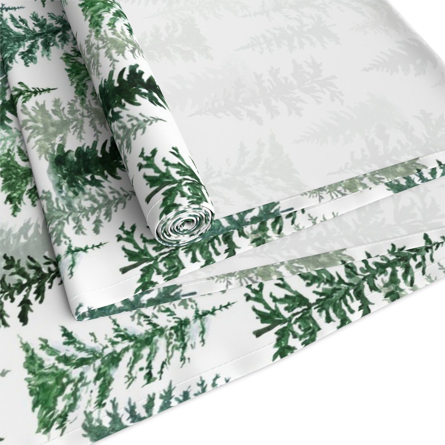 Green and white forest-themed cotton table runner rolled up and folded on a white background