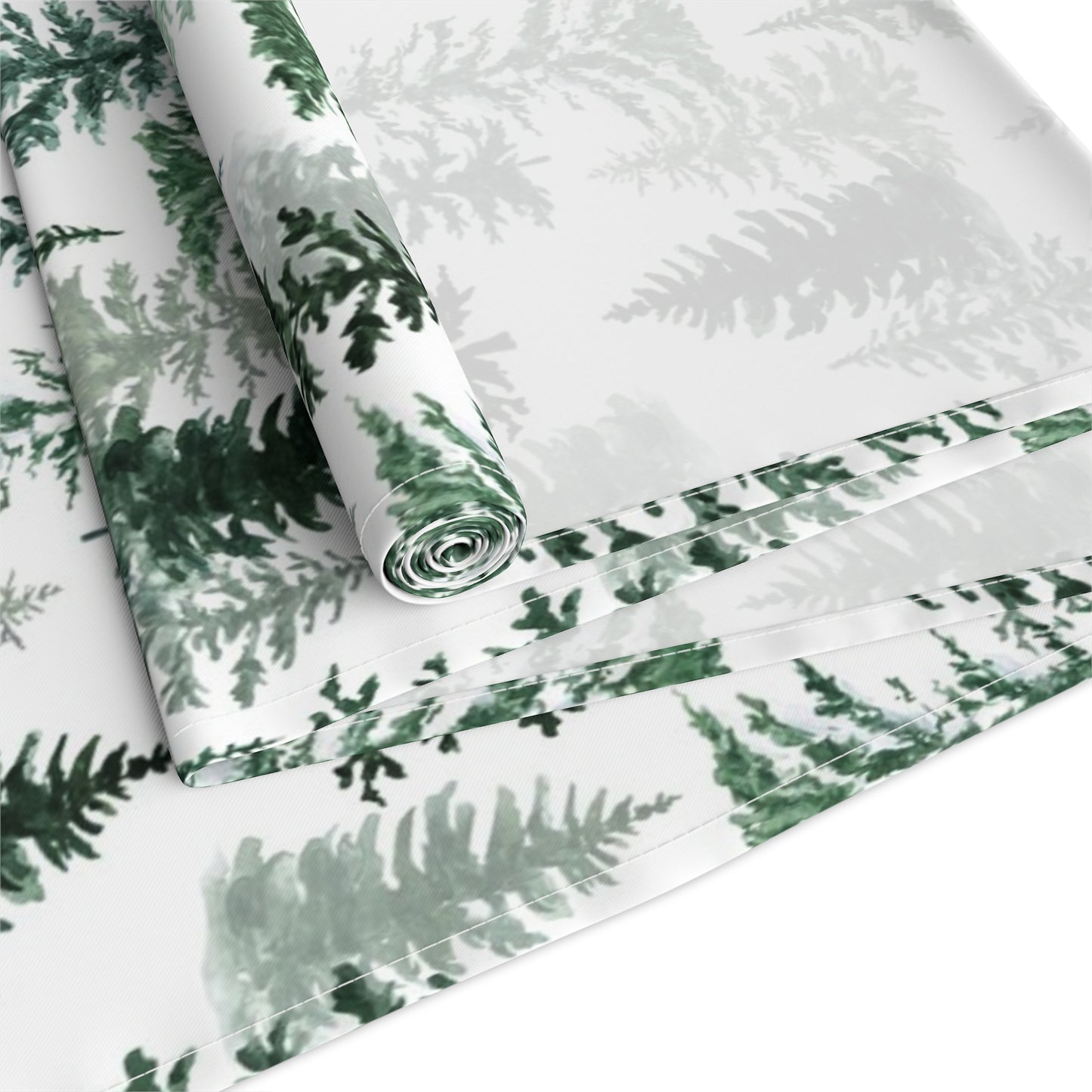 Green and white forest-themed cotton table runner rolled up and folded on a white background