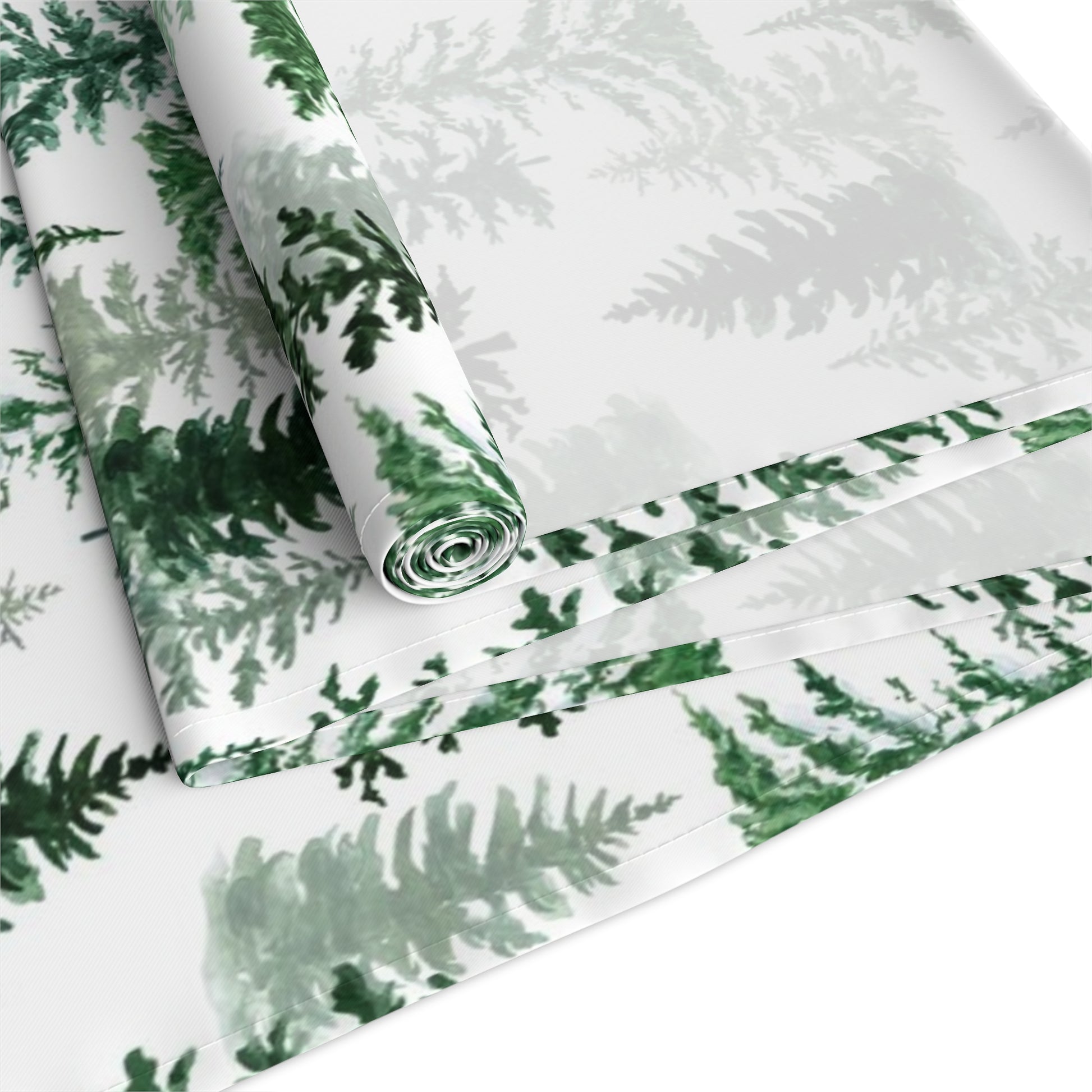 Green and white forest-themed cotton table runner rolled up and folded on a white background