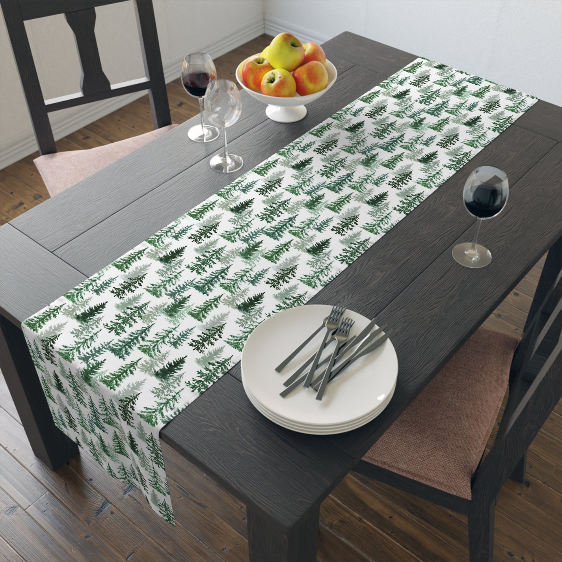 Table setting with a green and white forest-themed table runner on a wooden table with dishes, wine glasses and fruit bowl.