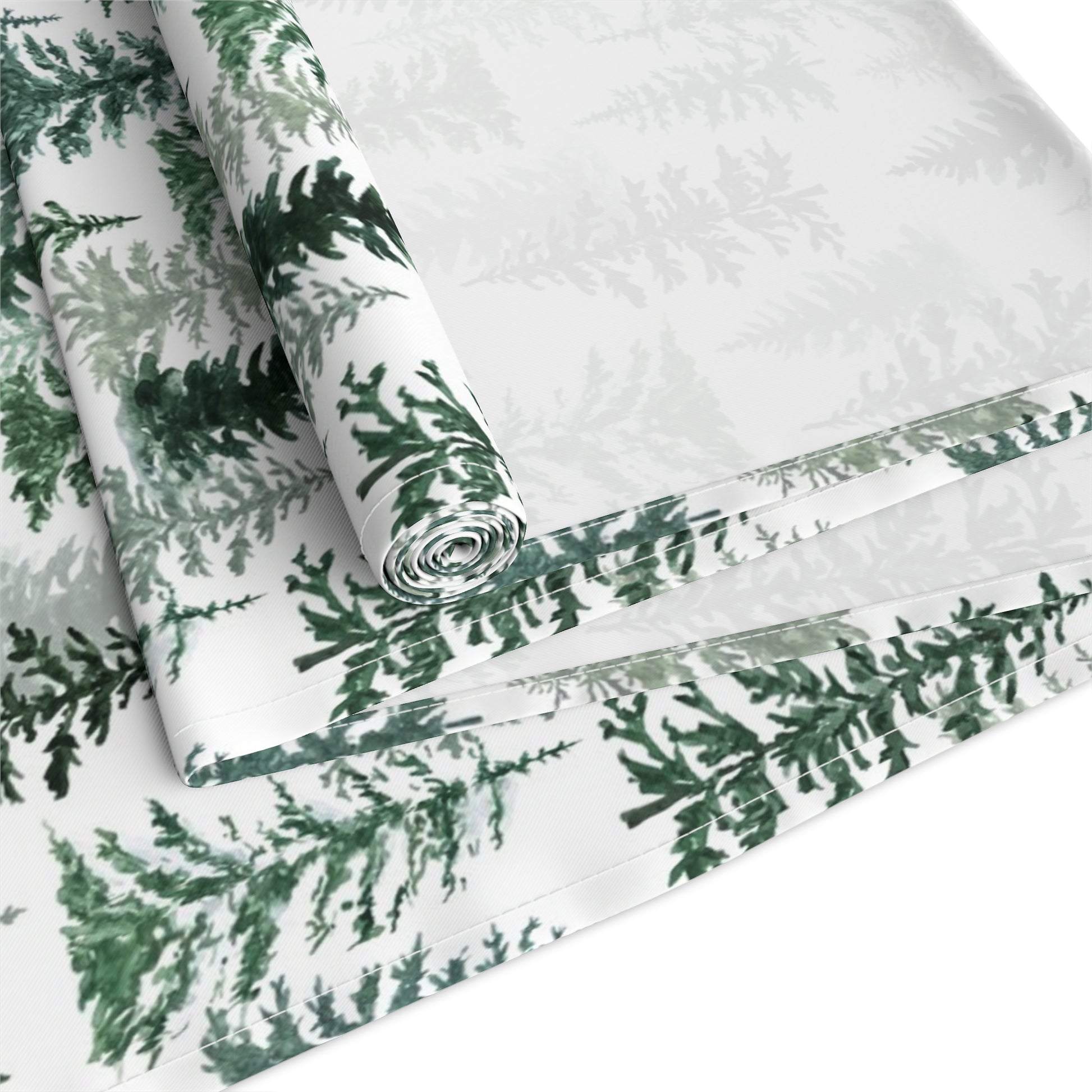 Green and white forest-themed cotton table runner rolled up and folded on a white background