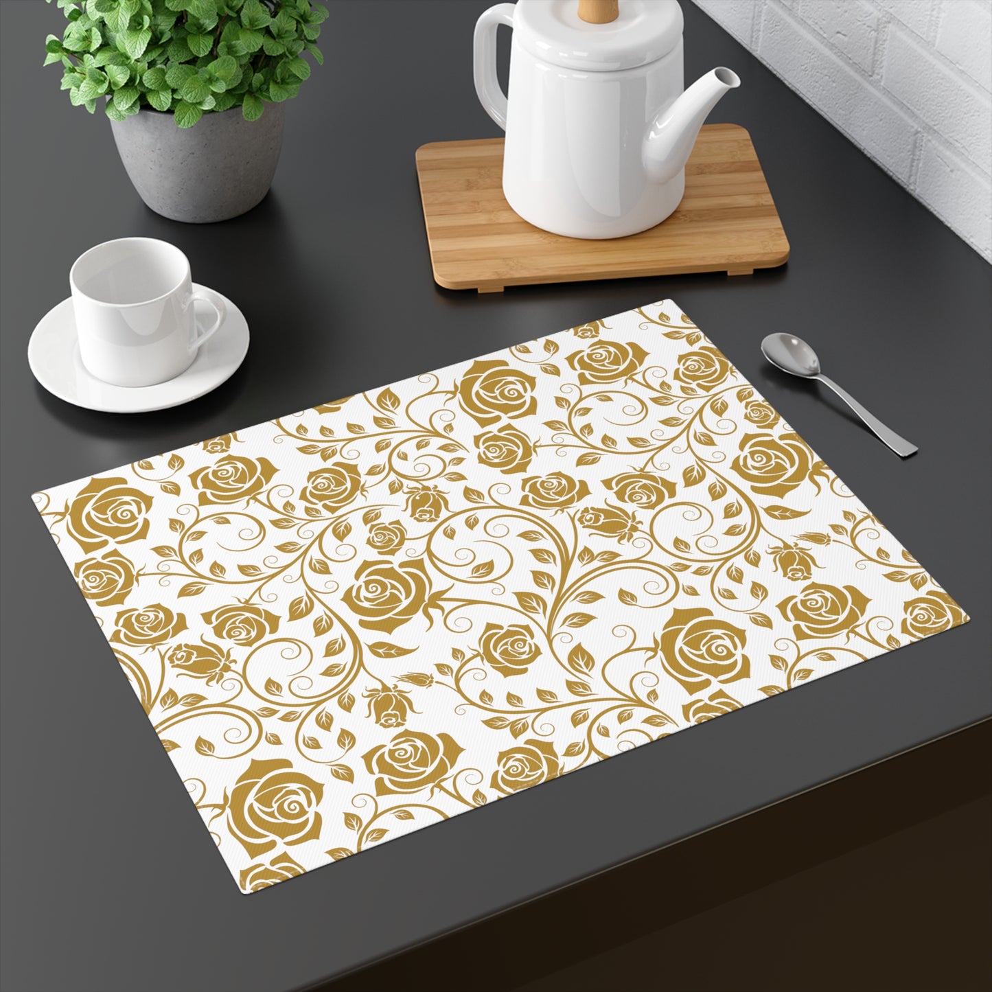 Placemat with gold rose pattern on a dark surface with tea set and plant.