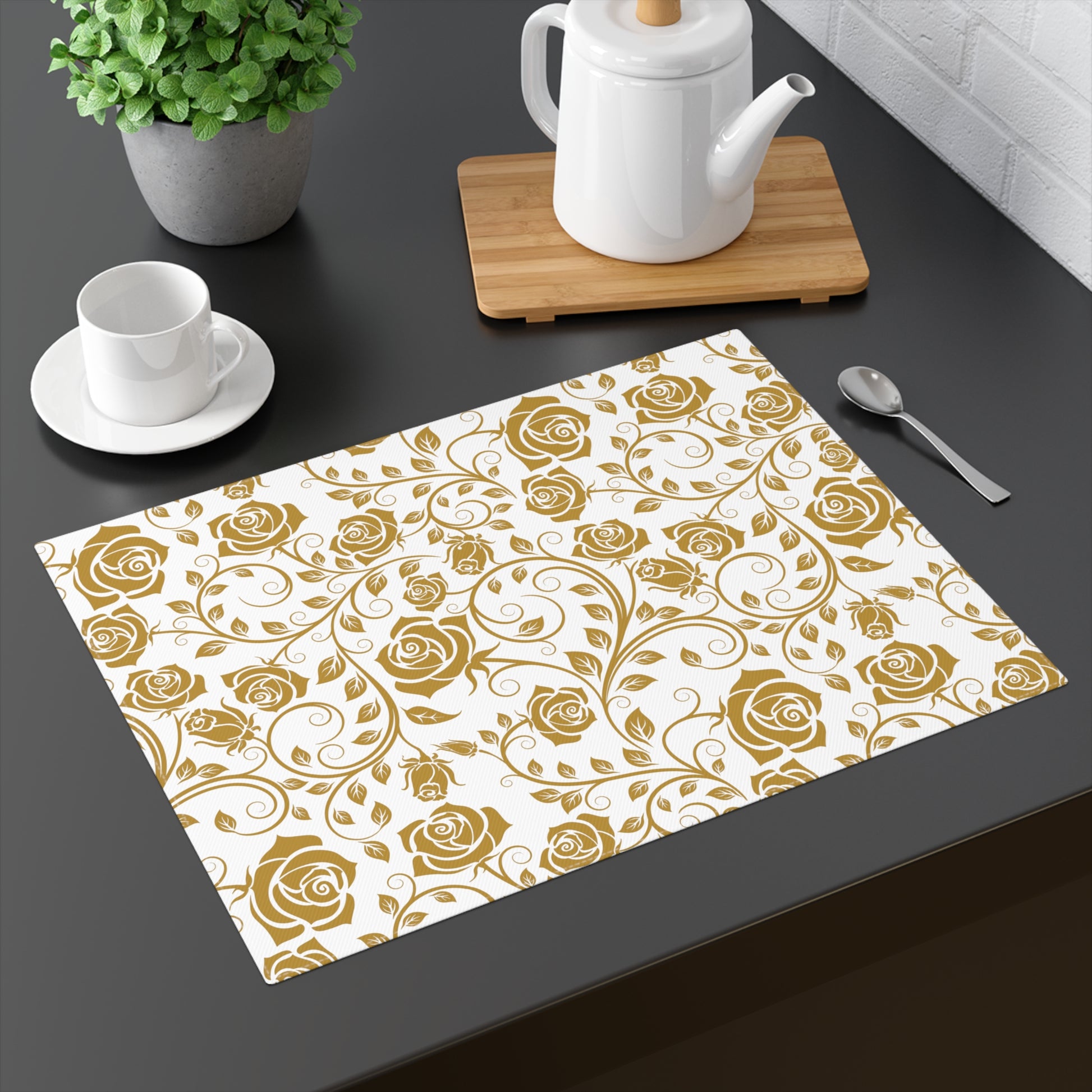 Placemat with gold rose pattern on a dark surface with tea set and plant.