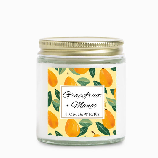 Grapefruit and Mango scented candle in a clear jar with gold lid with a decorative mangoes label on a white background by Home & Wicks