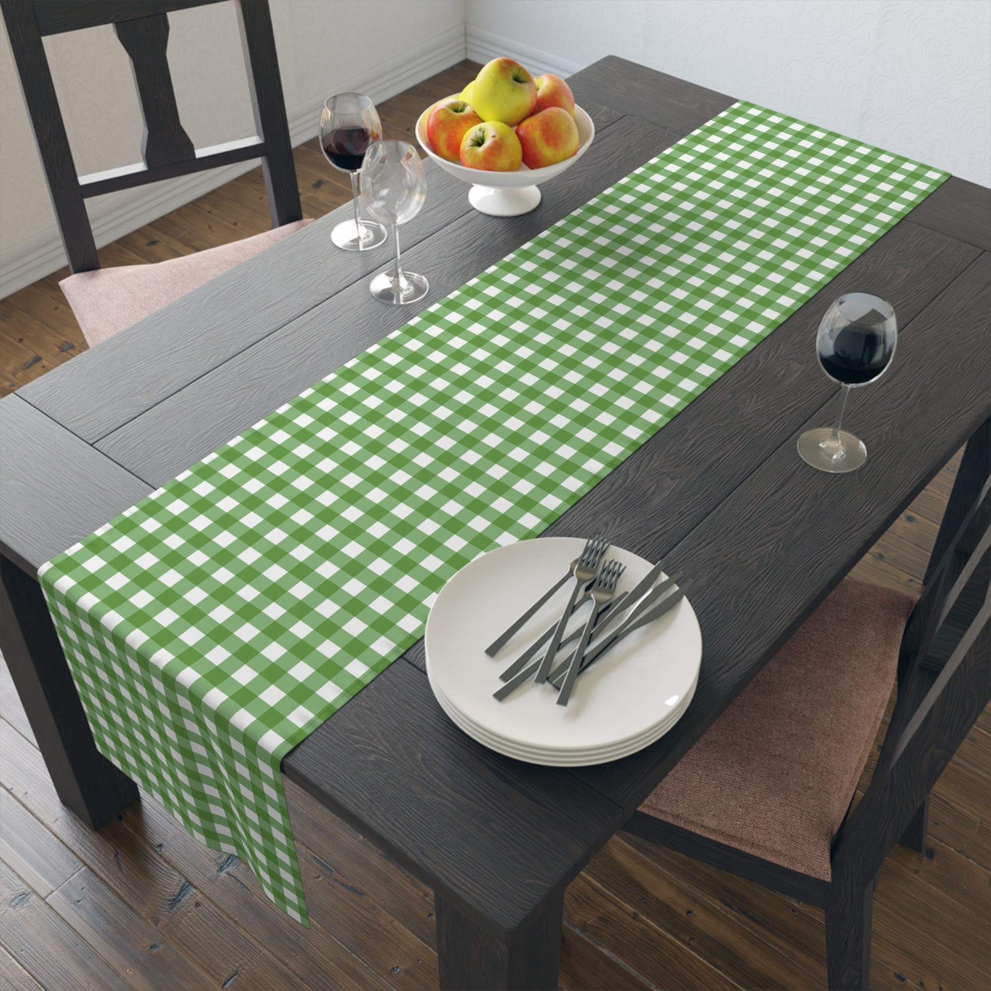 Green gingham checkered table runner with green and white gingham pattern printed on front of table runner, sitting on a dark table with dishes, wine glass and fruit bowl.