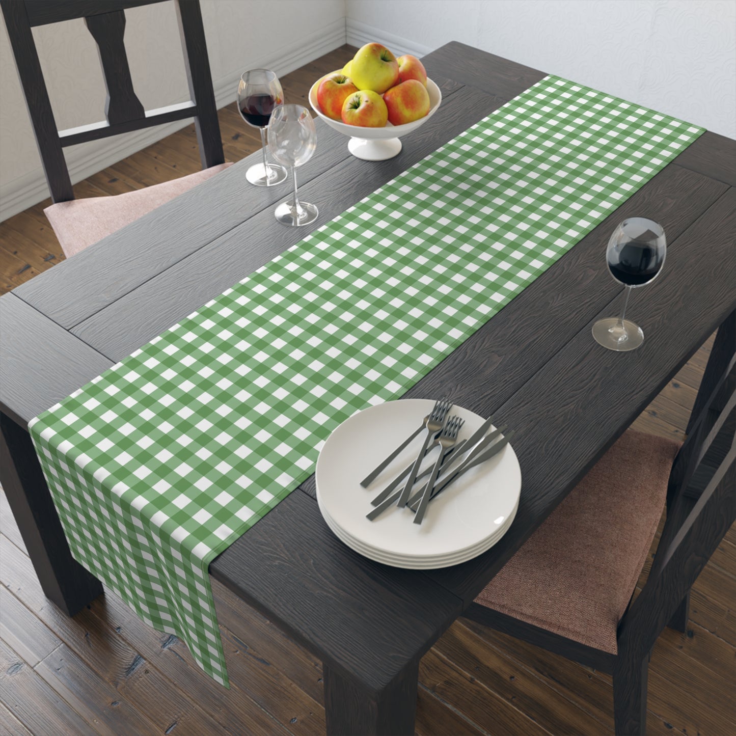 Green gingham checkered table runner with green and white gingham pattern printed on front of table runner, sitting on a dark table with dishes, wine glass and fruit bowl.