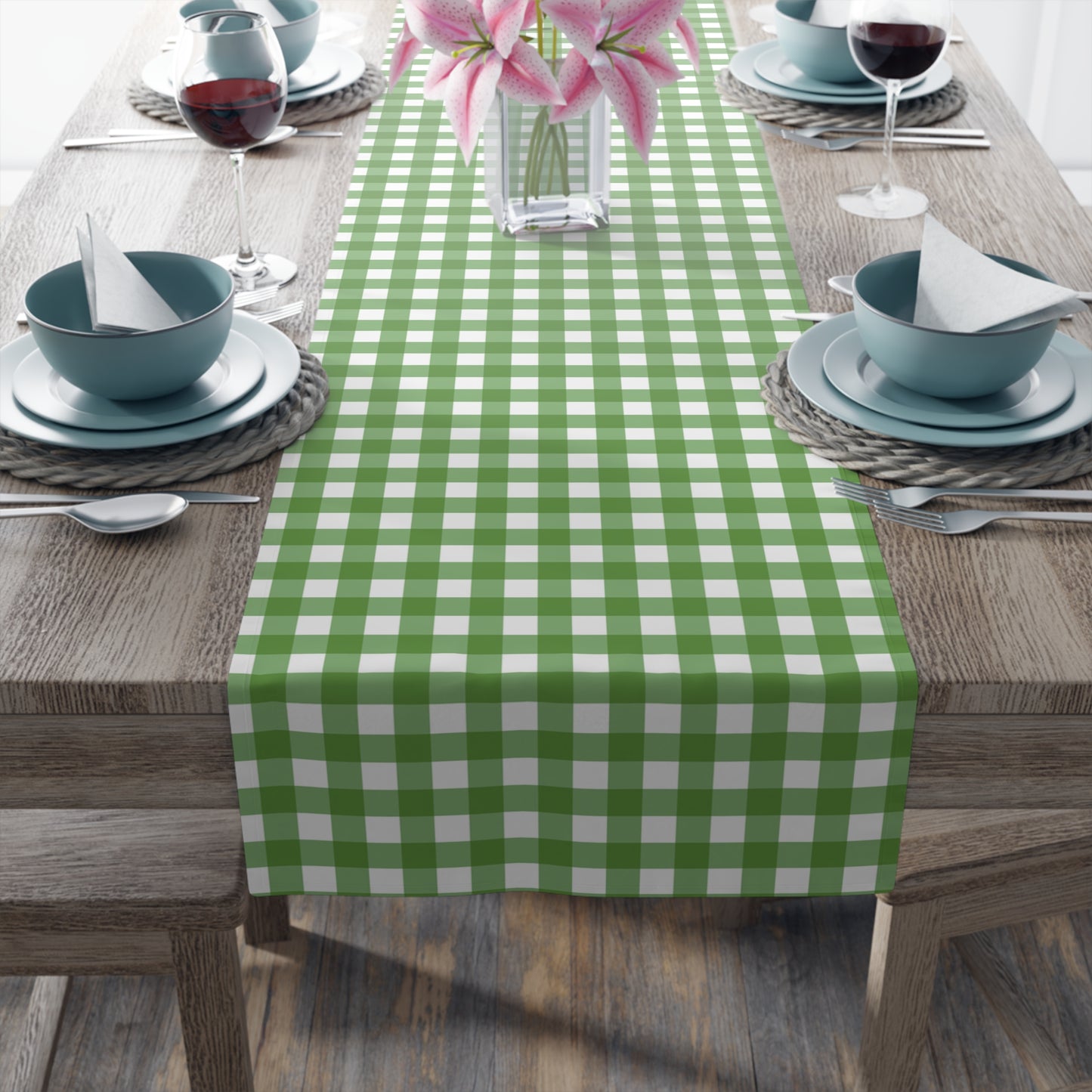 Close up view of green gingham checkered table runner with green and white gingham pattern printed on front of table runner, on a brown table with place settings.