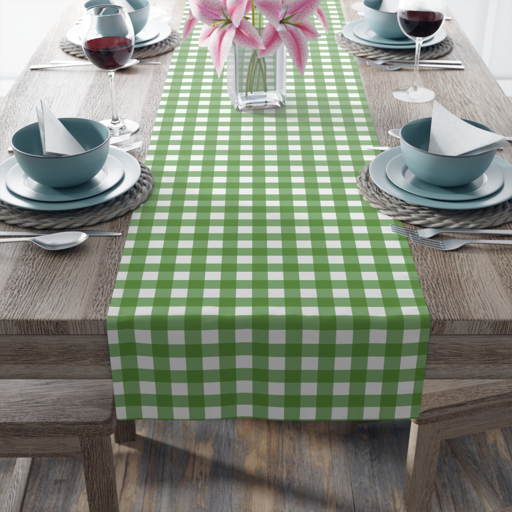 Close up view of green gingham checkered table runner with green and white gingham pattern printed on front of table runner, on a brown table with place settings.