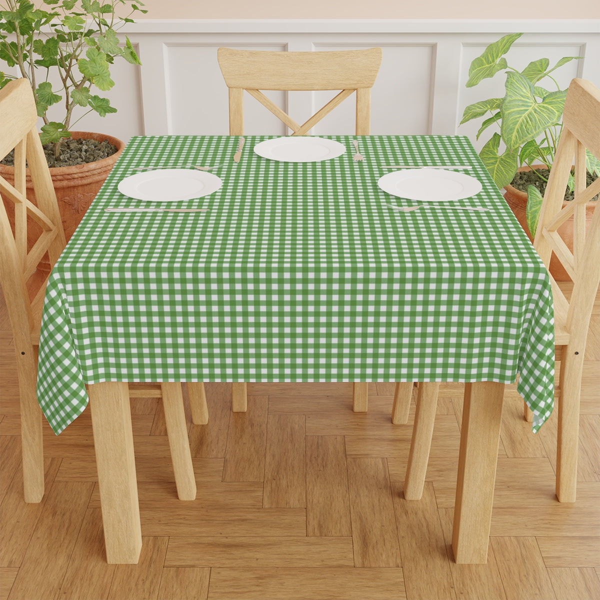 Dining table with a green Green and white gingham checkered tablecloth, white plates, and wooden chairs.