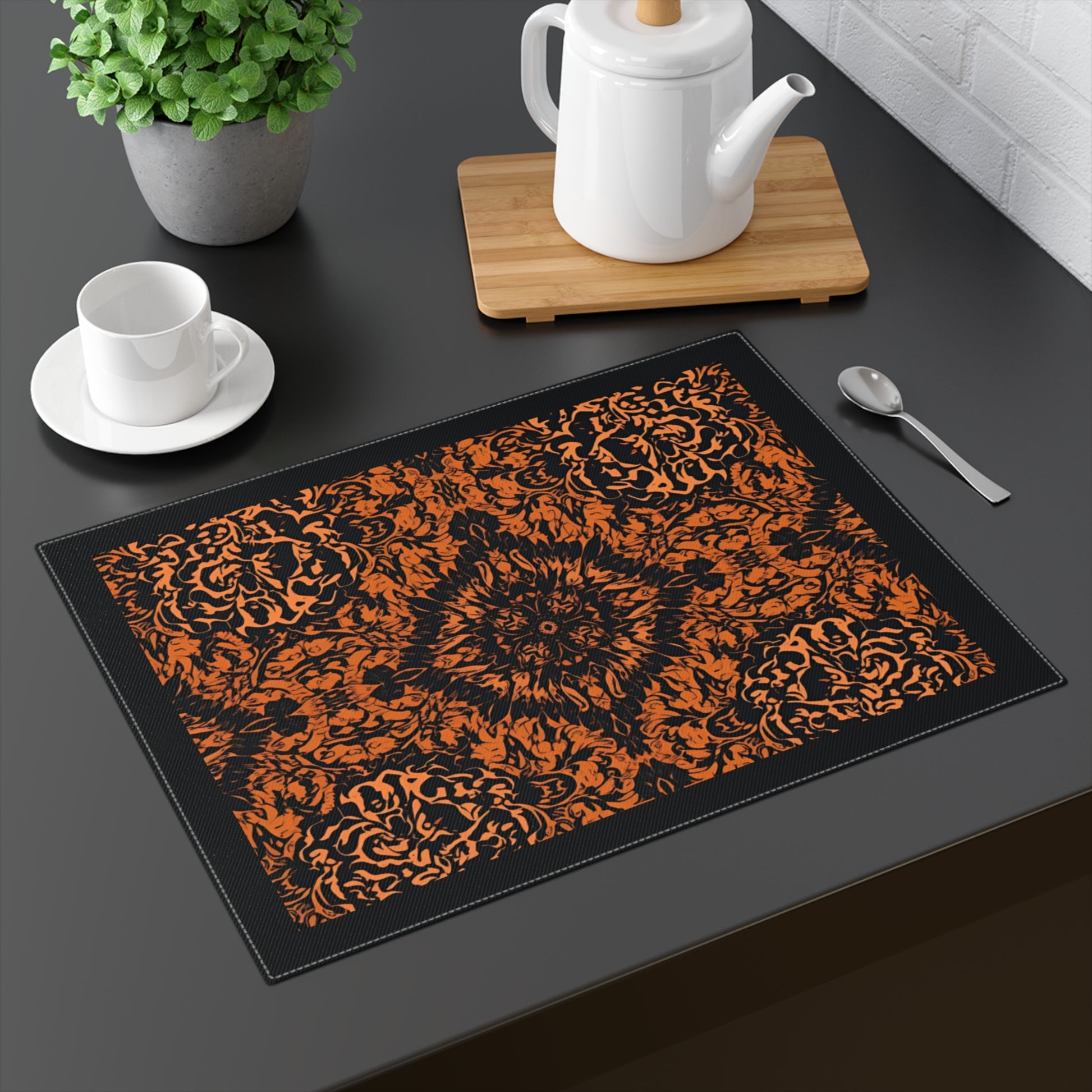 Groovy Black & Orange placemat with intricate black and orange pattern printed on the cotton twill placemat that is set on a dark colored table with tea cup and tea pot.