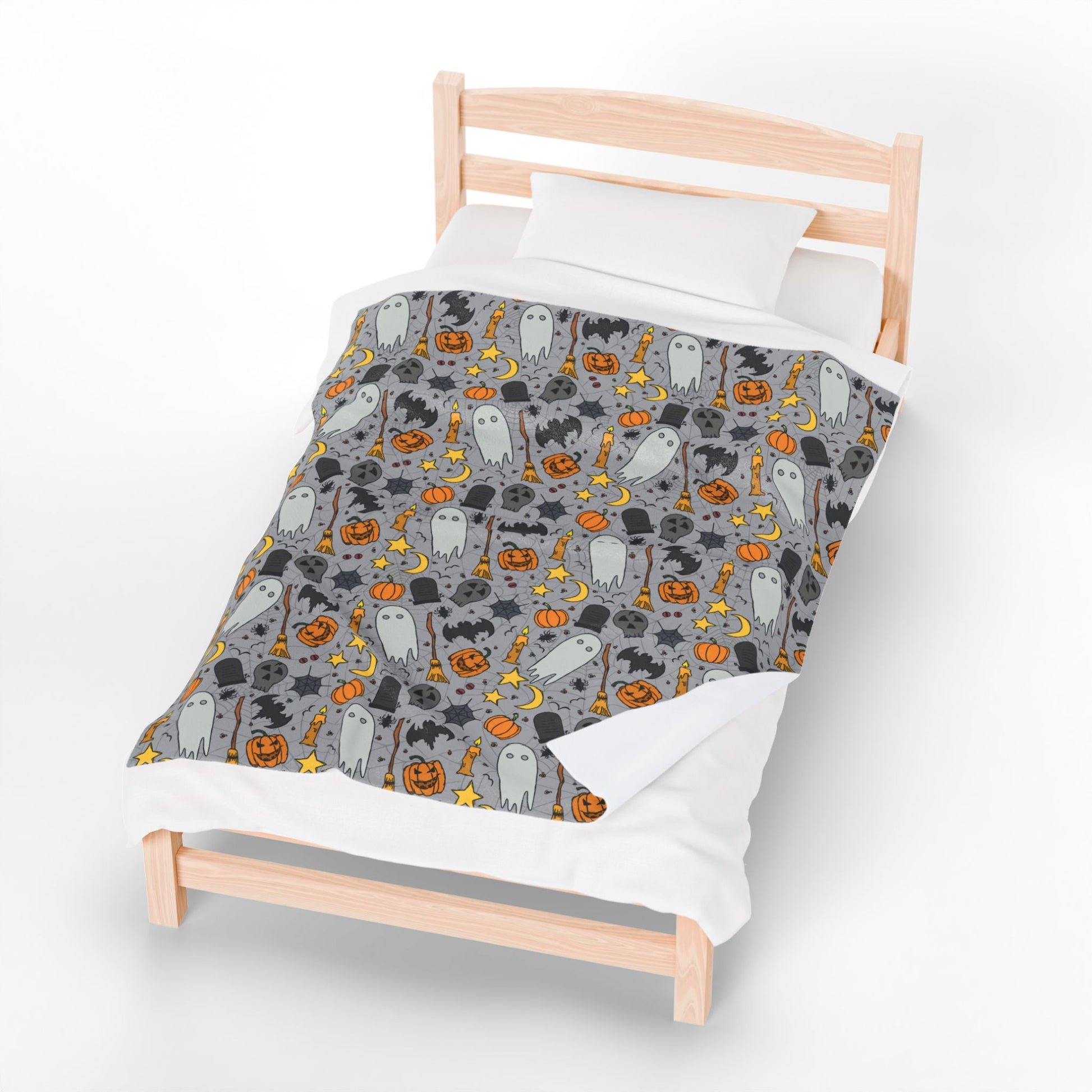 Halloween-themed patterned blanket with ghosts, pumpkins, and stars on a gray background on front of blanket, on a small bed with a white background