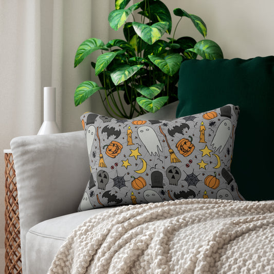 Halloween-themed lumbar pillow with ghost, pumpkin, and broomstick design printed on front and back of pillow cover with a gray background, on a couch with a plant in the background