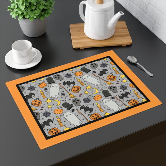 Halloween-themed placemat with ghosts, pumpkins, and bats on a gray background with an orange border, on a dark table with a teapot and cup in the background.