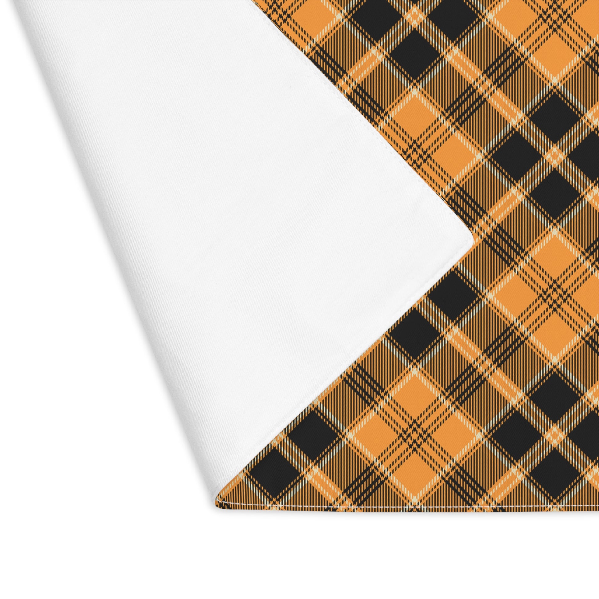 Halloween Plaid placemat has plaid pattern in orange and black colors printed on top of placemat, one corner is lifted to reveal white backside on a white background.