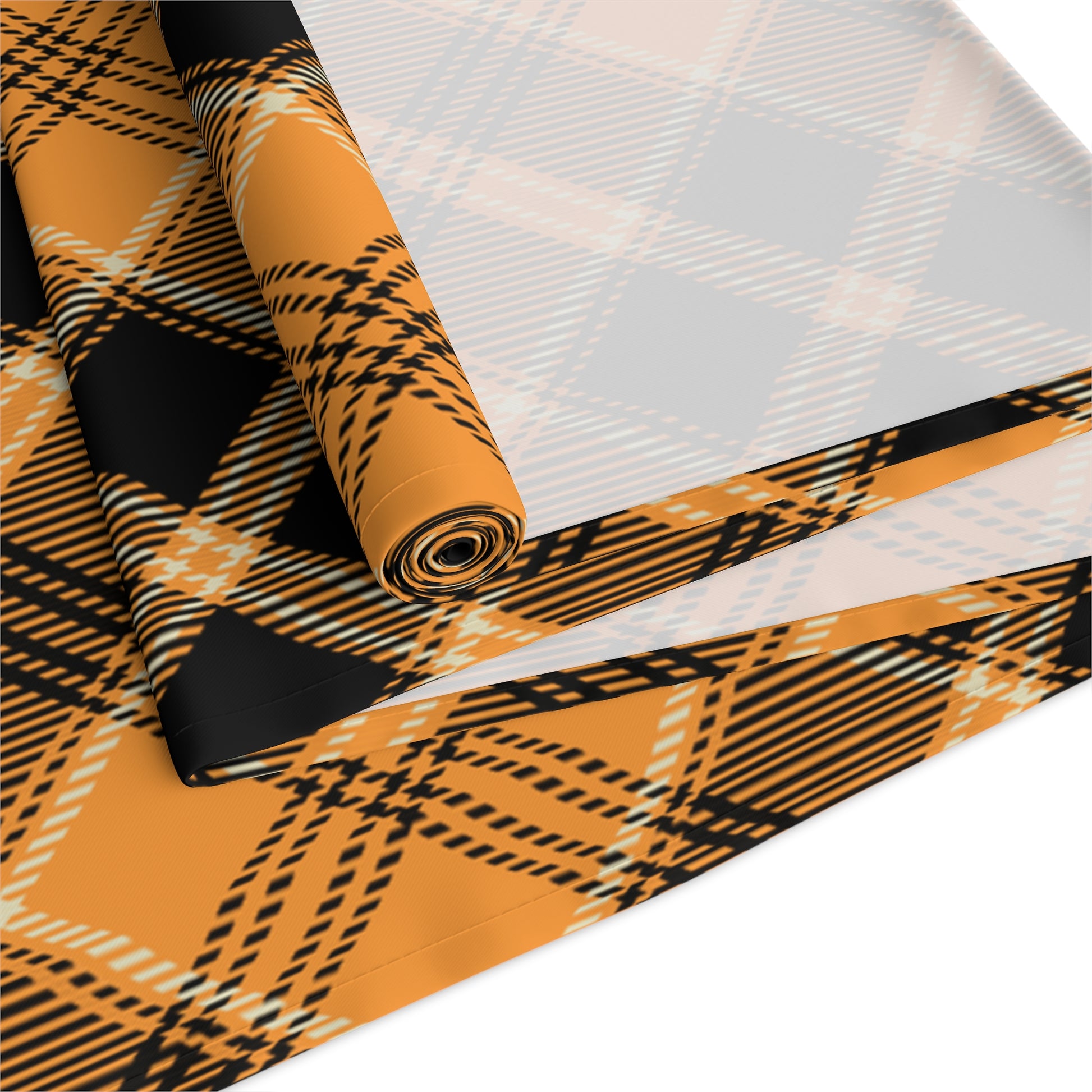 Pumpkin plaid table runner has a black and orange plaid pattern on front of table runner, rolled up and folded on a white background.