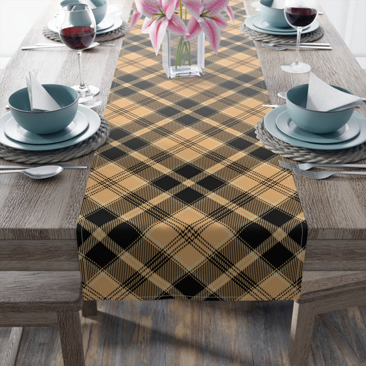 Pumpkin plaid table runner has a black and orange plaid pattern on front of table runner, on a wooden table with place settings.