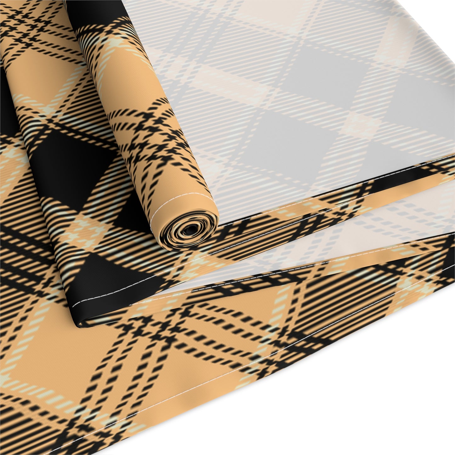 Pumpkin plaid table runner has a black and orange plaid pattern on front of table runner, rolled up and folded on a white background.