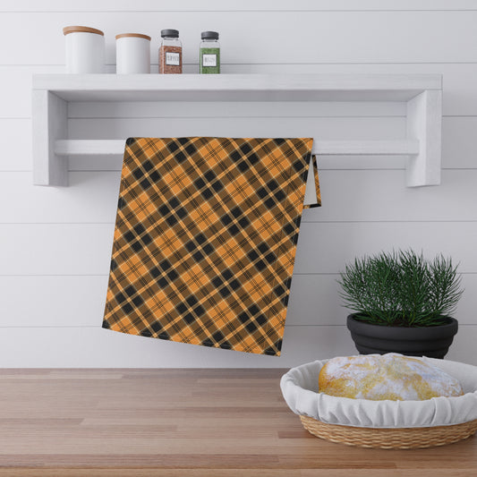 Orange and black plaid tea kitchen towel hanging on a wooden shelf towel rack with a plant and basket in the foreground