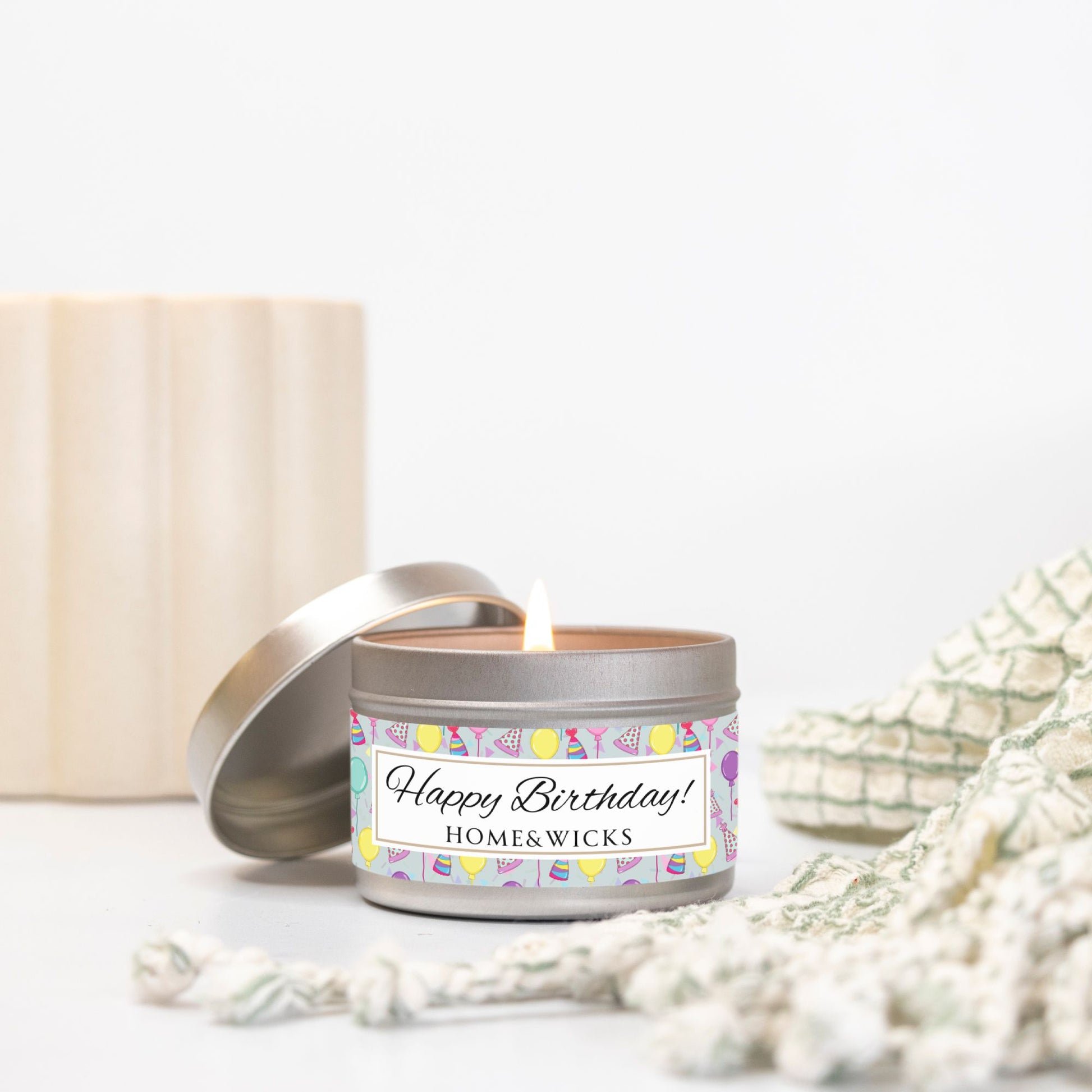 Happy Birthday silver candle 4 oz. tin with 'Happy Birthday' label with colorful design of birthday hats, balloons and confetti on a light background