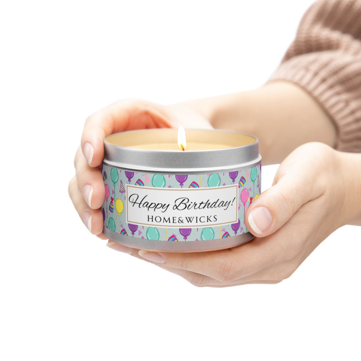 Person holding a silver candle tin with 'Happy Birthday' label and colorful balloon, birthday hats and confetti design 