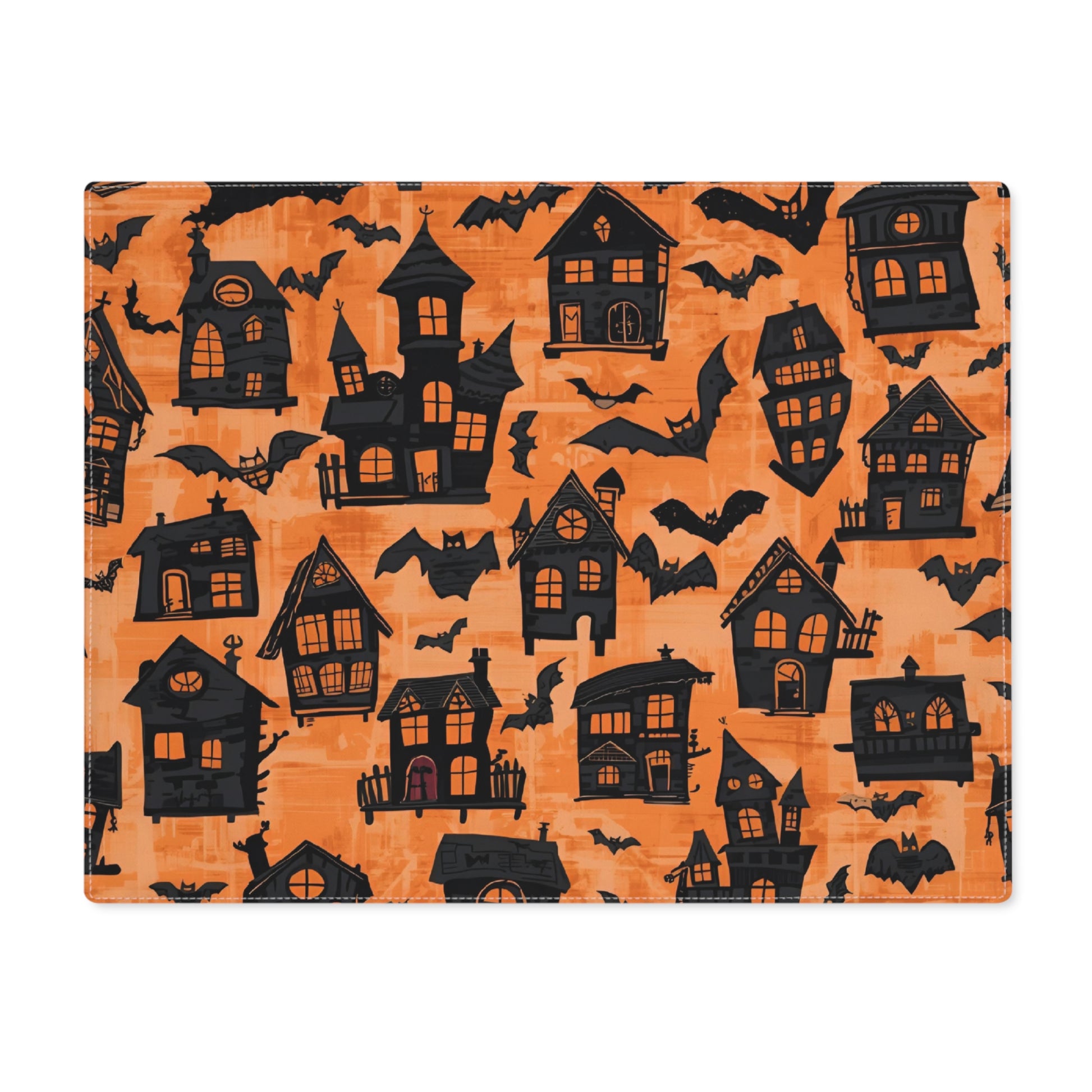 Halloween-themed placemat with black haunted houses and bats on an orange background. The placemat sits on a white background.