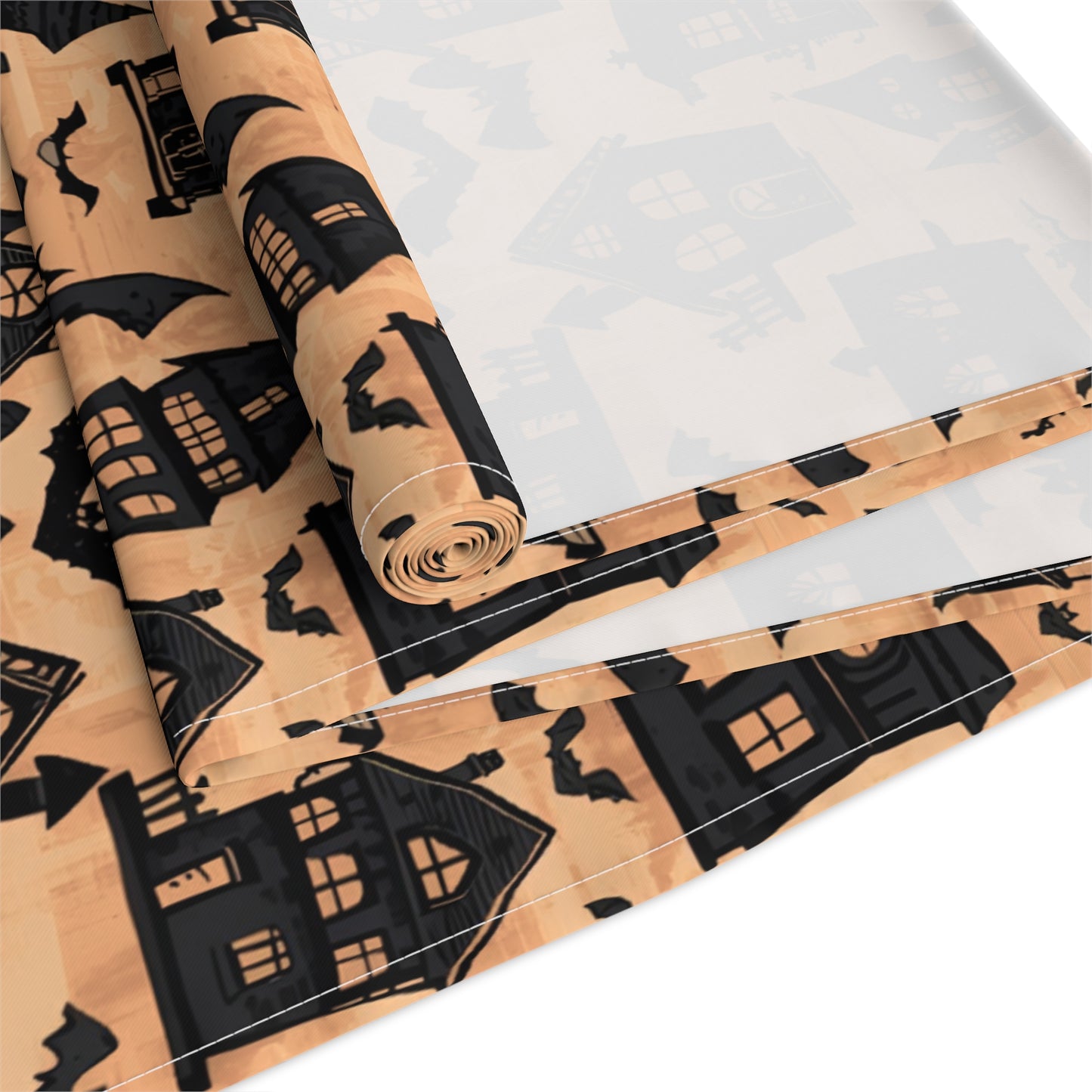 Halloween-themed table runner with black haunted houses and bat patterns on an orange background. This Haunted Houses table runner is rolled up on a white background.
