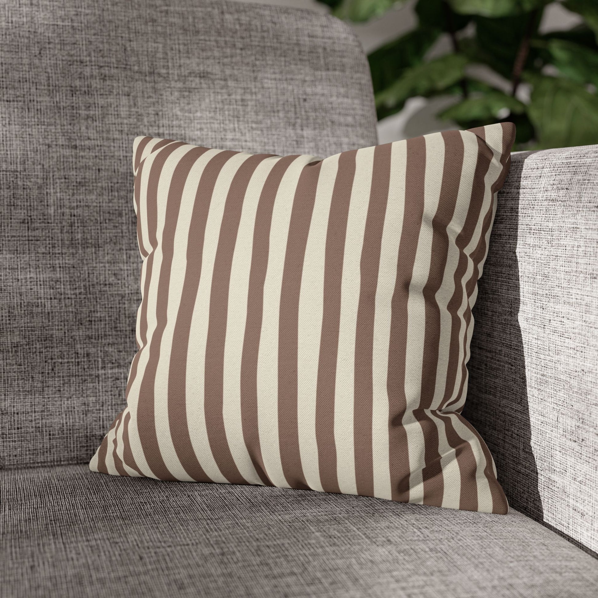 Mocha brown striped pillow on a gray sofa with a blurred plant in the background
