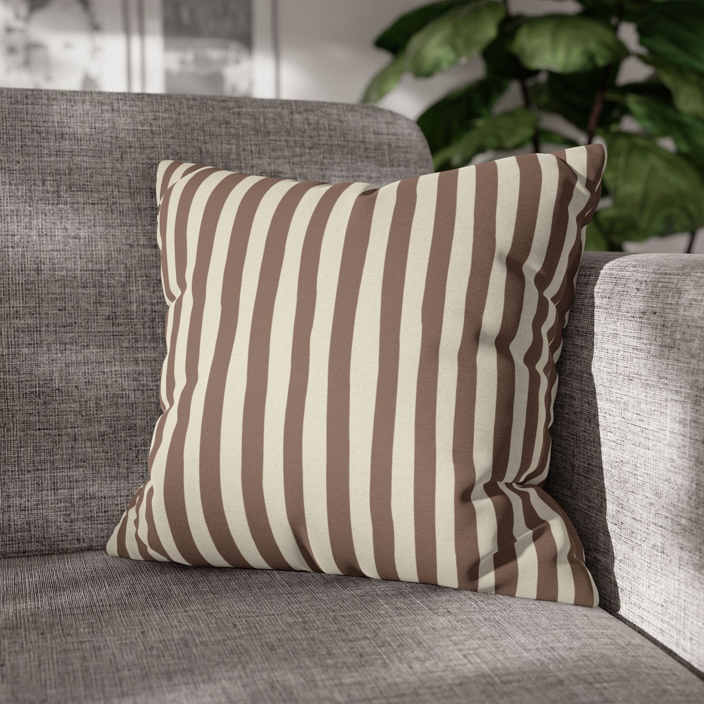Mocha brown striped pillow on a gray sofa with a blurred plant in the background